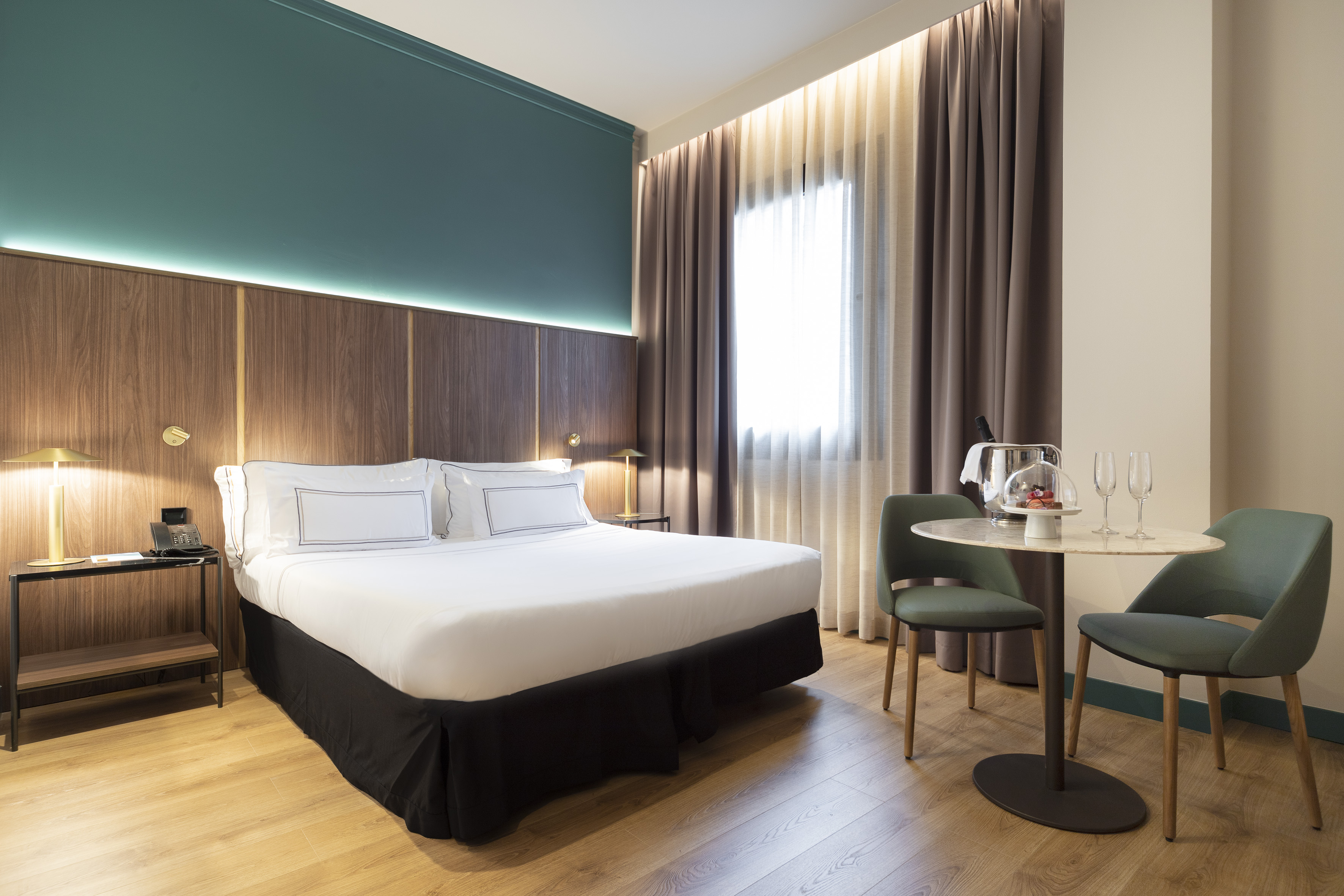 Modern hotel room with queen bed, teal accent wall, and champagne setup.