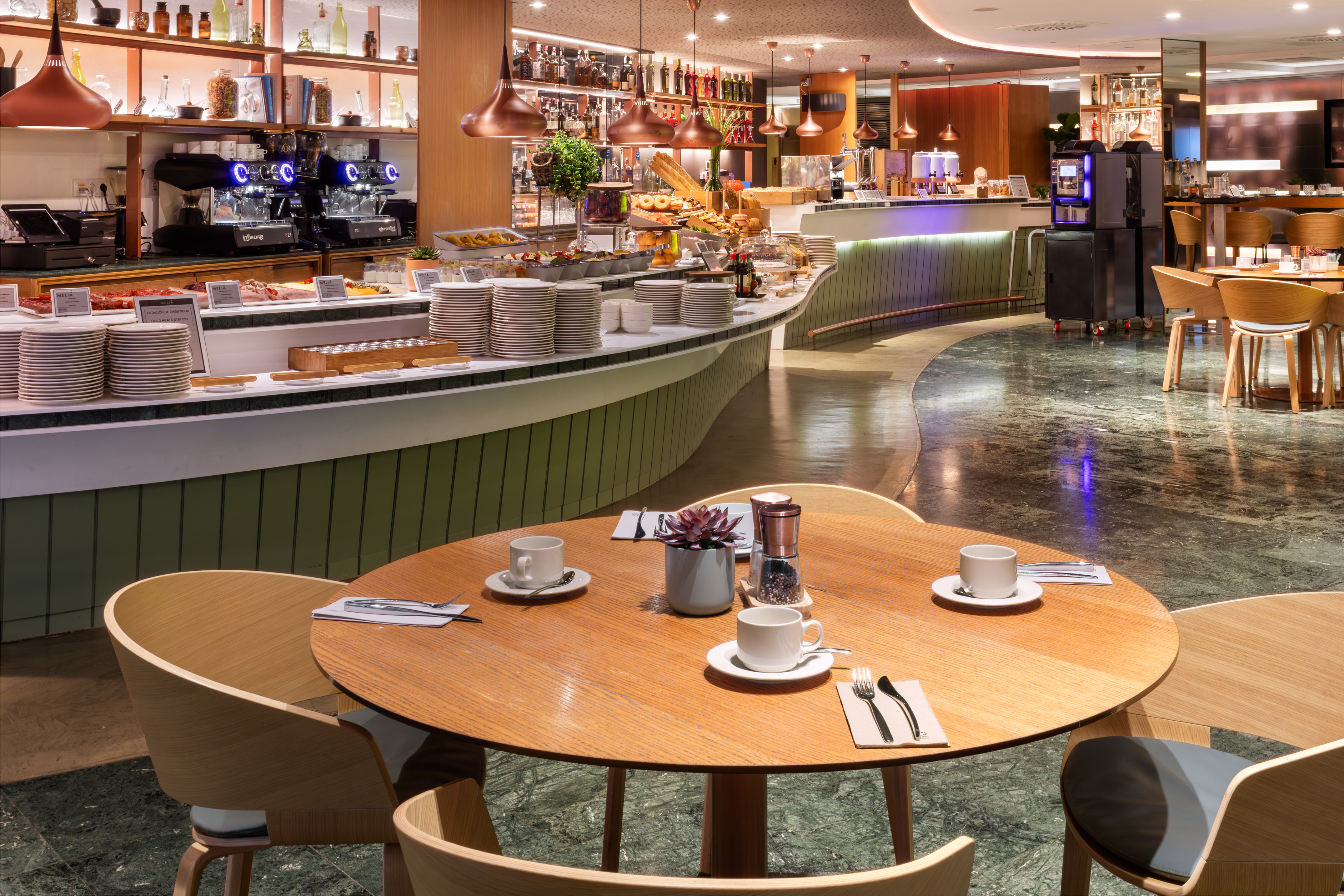 Modern hotel breakfast buffet with food, coffee machines, and dining tables.
