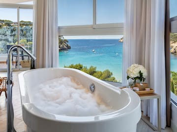 a bathtub with bubbles in front of a window overlooking a body of water