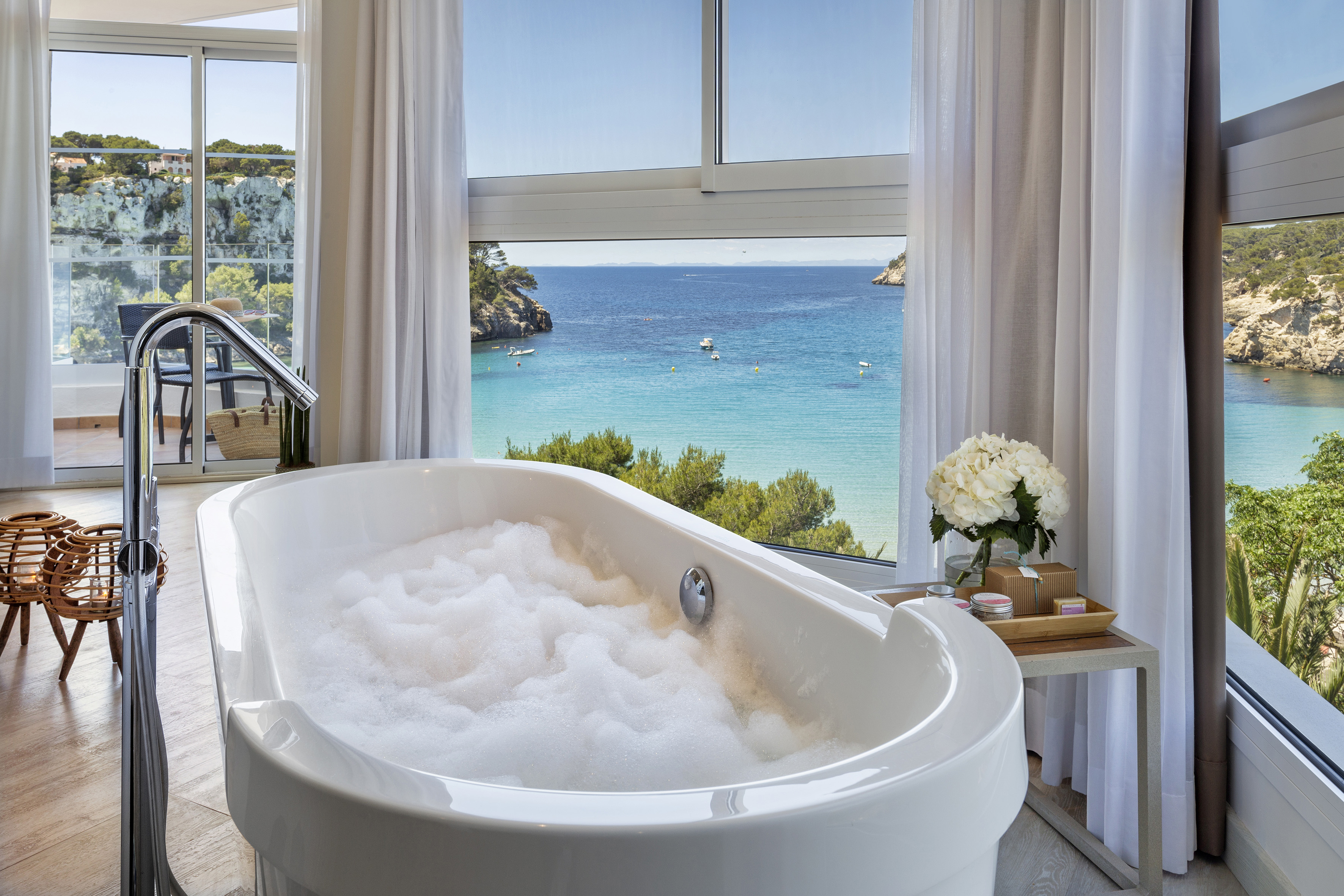 a bathtub with bubbles in front of a window overlooking a body of water