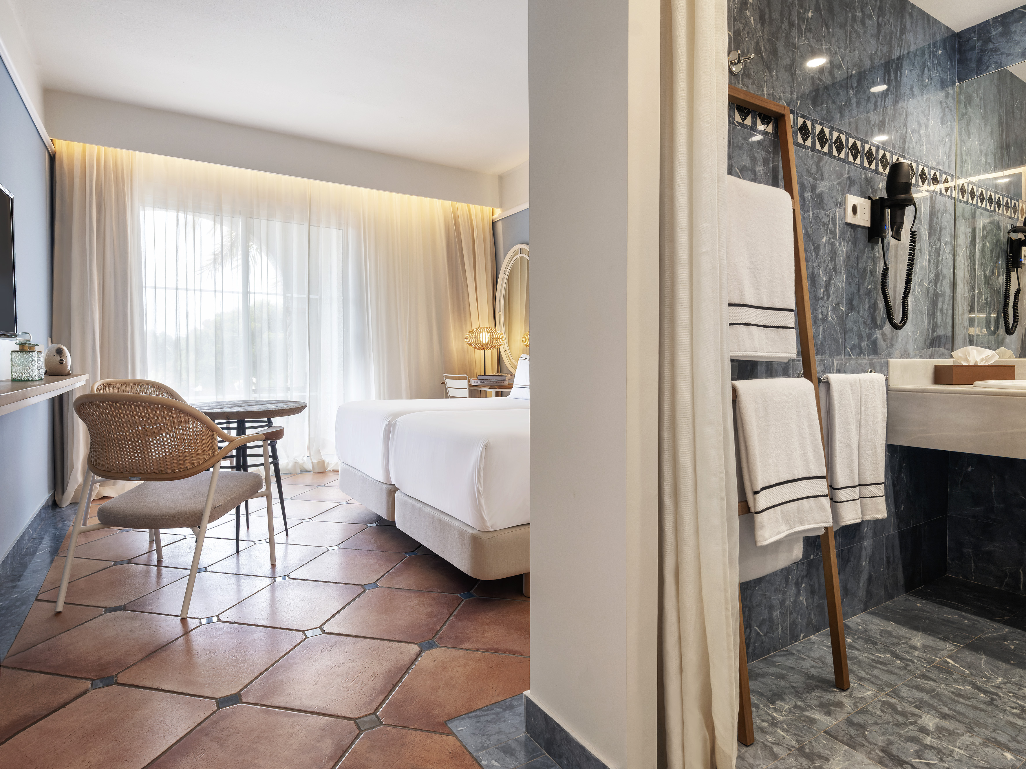 Hotel room with twin beds, terracotta floor, and dark marble bathroom.