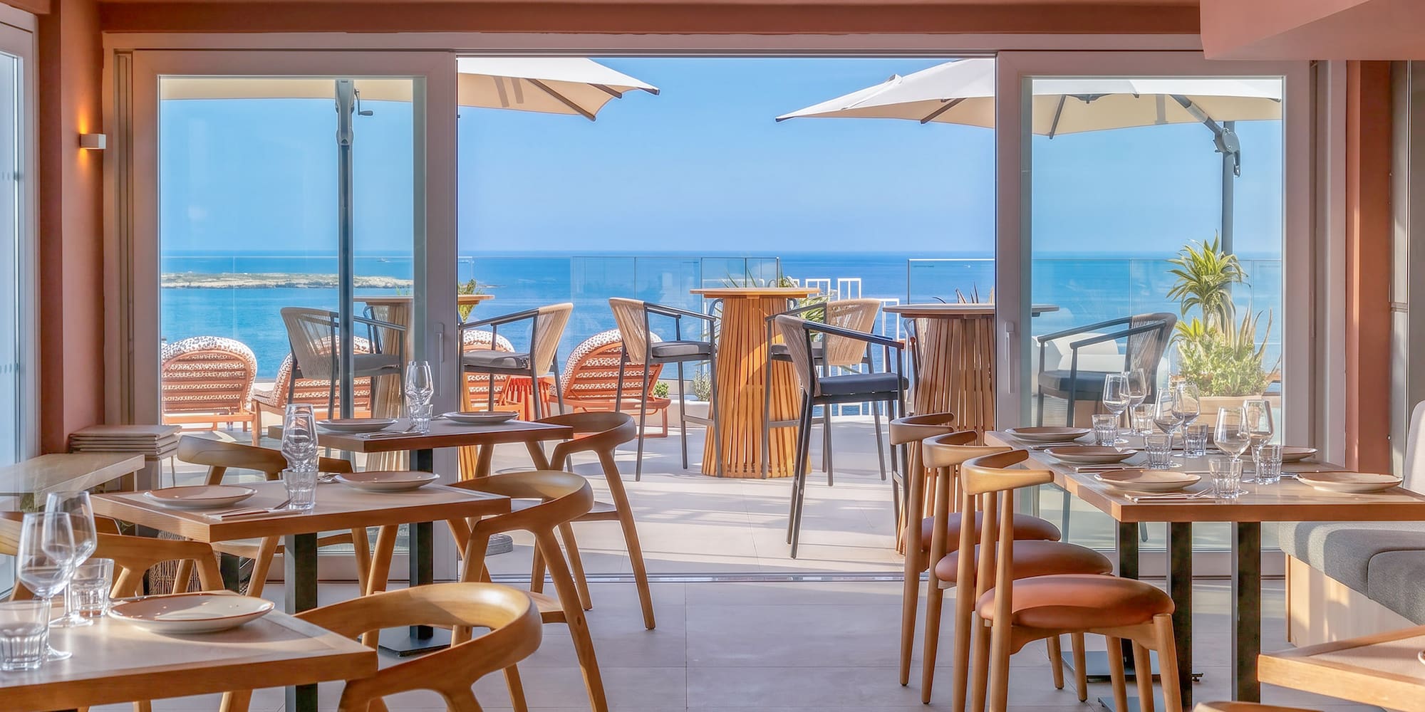 Modern restaurant dining area, set tables, with outdoor sea view terrace.