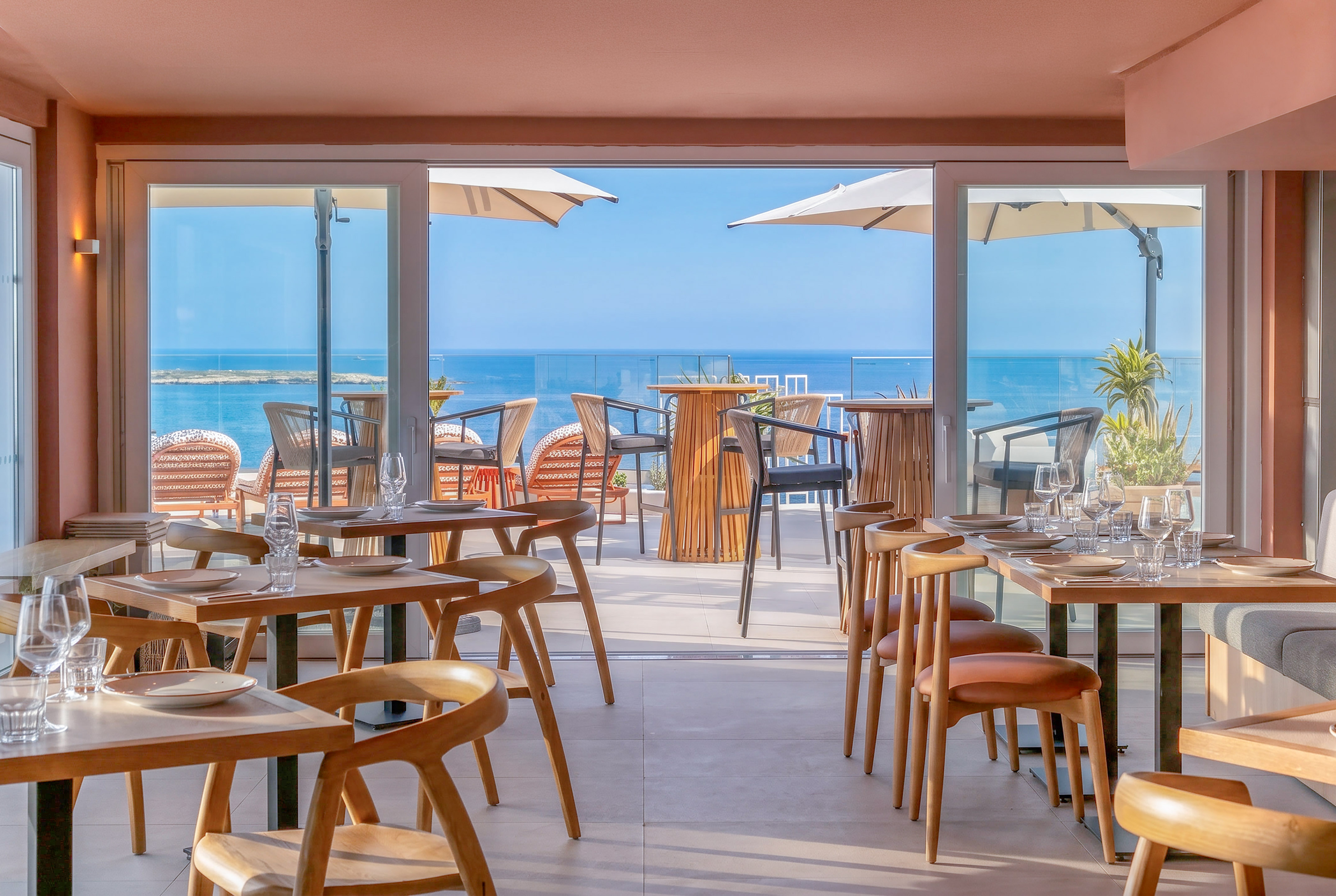 Dining room overlooking ocean, with set tables and an outdoor terrace.