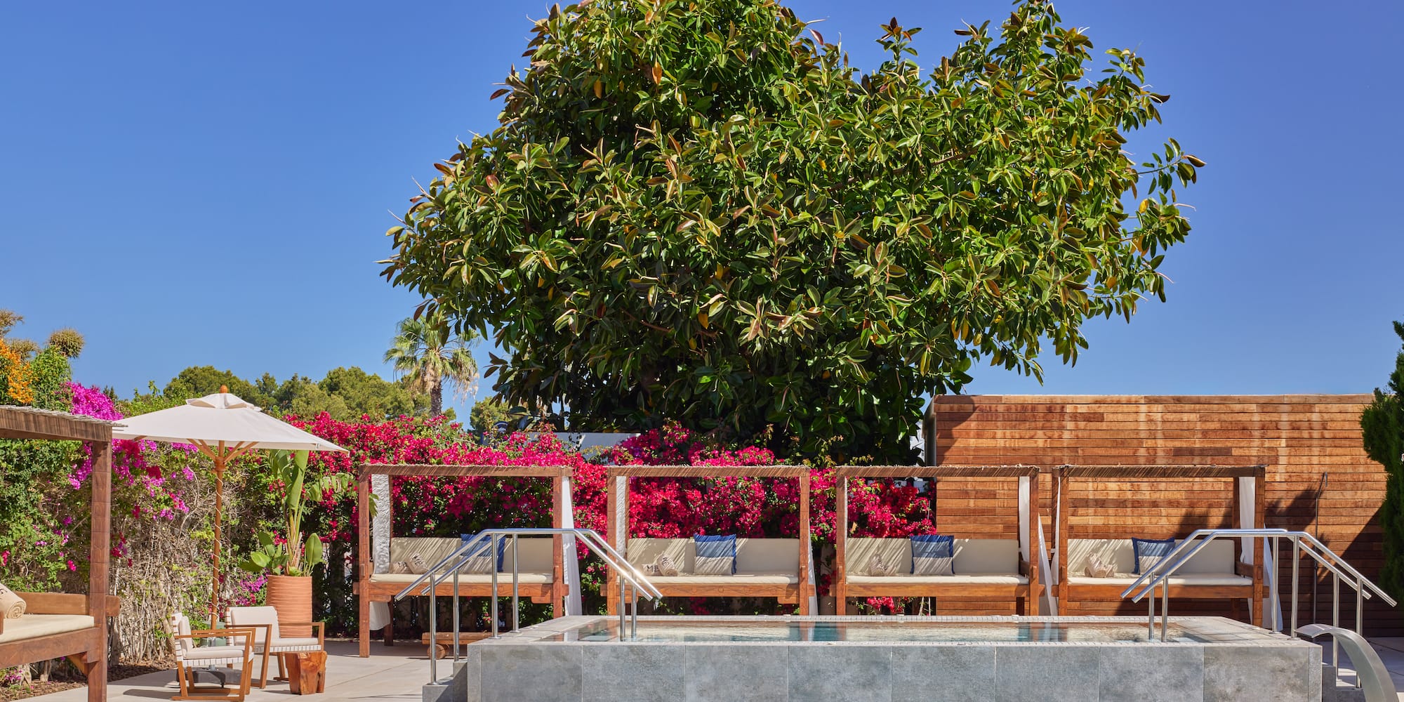 Luxury resort pool area with cabanas, hot tub, and lush pink bougainvillea.