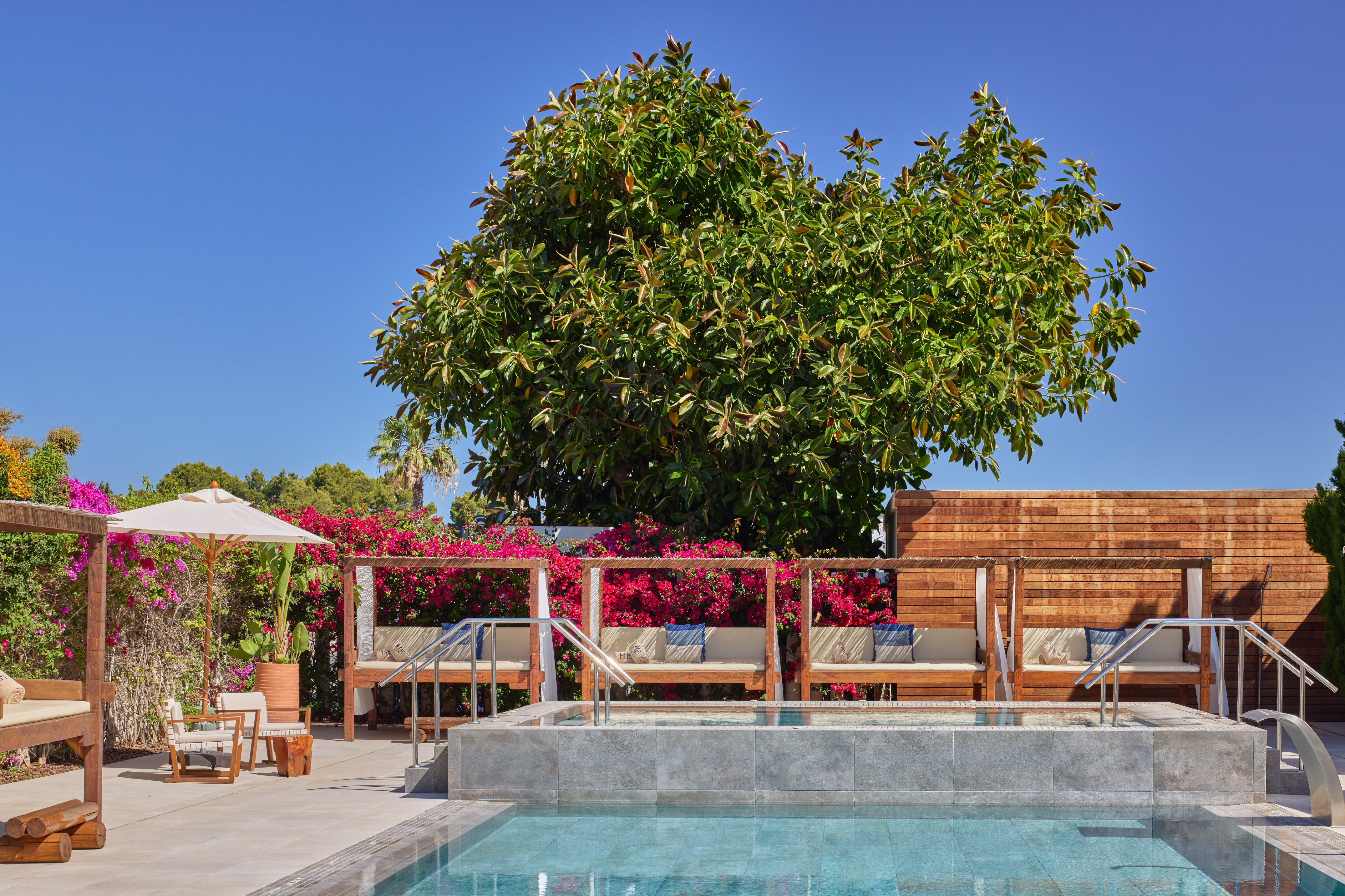 Resort swimming pool with wooden cabanas, hot tub, and vibrant bougainvillea.