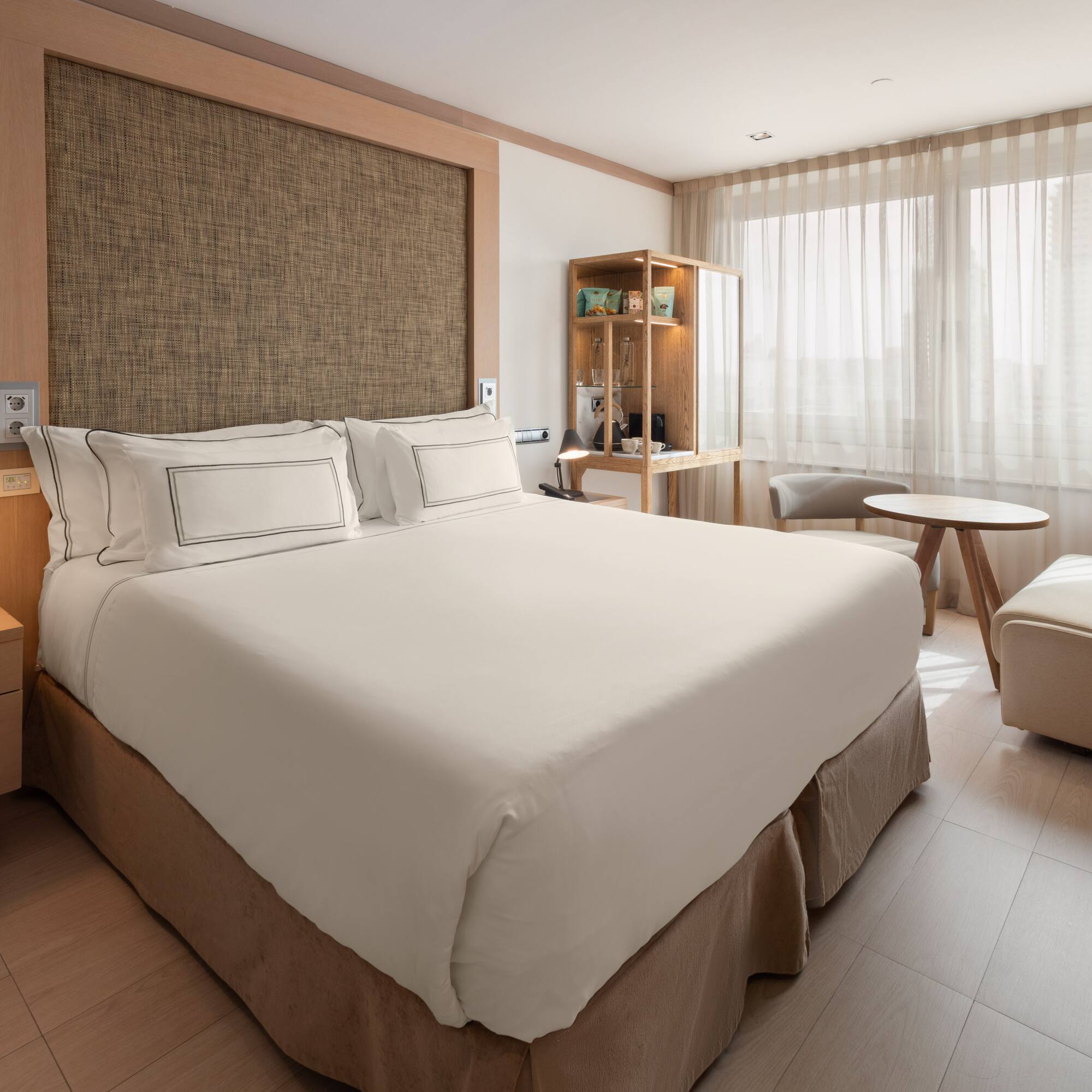 Modern hotel room with bed, wood accents, nightstand, and bright window.