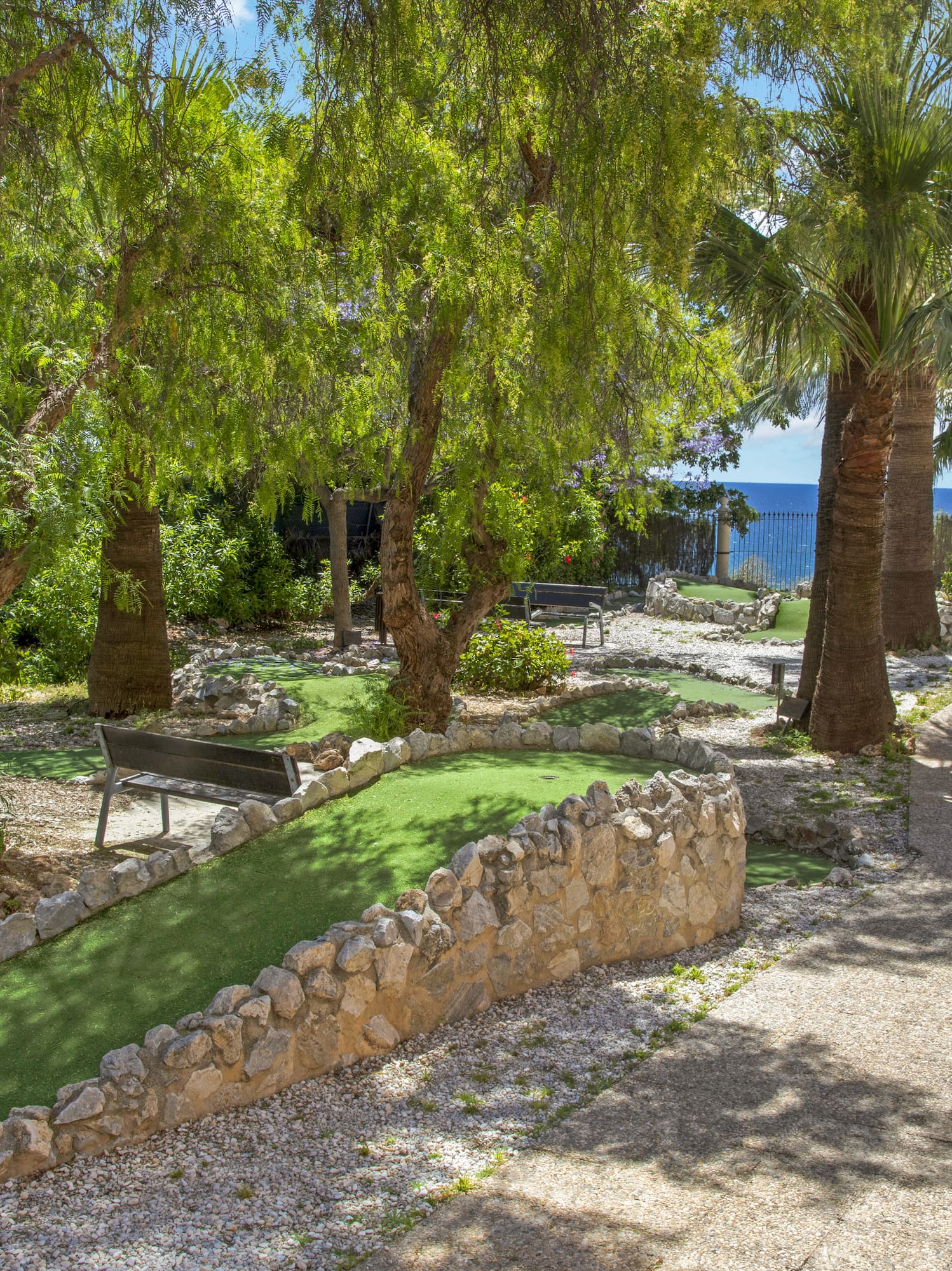 Mini golf course with green turf, palm trees, and a clear ocean view.