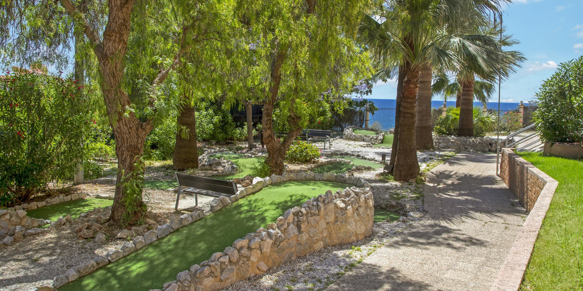 Mini-golf course with green turf, palm trees, and blue ocean view.