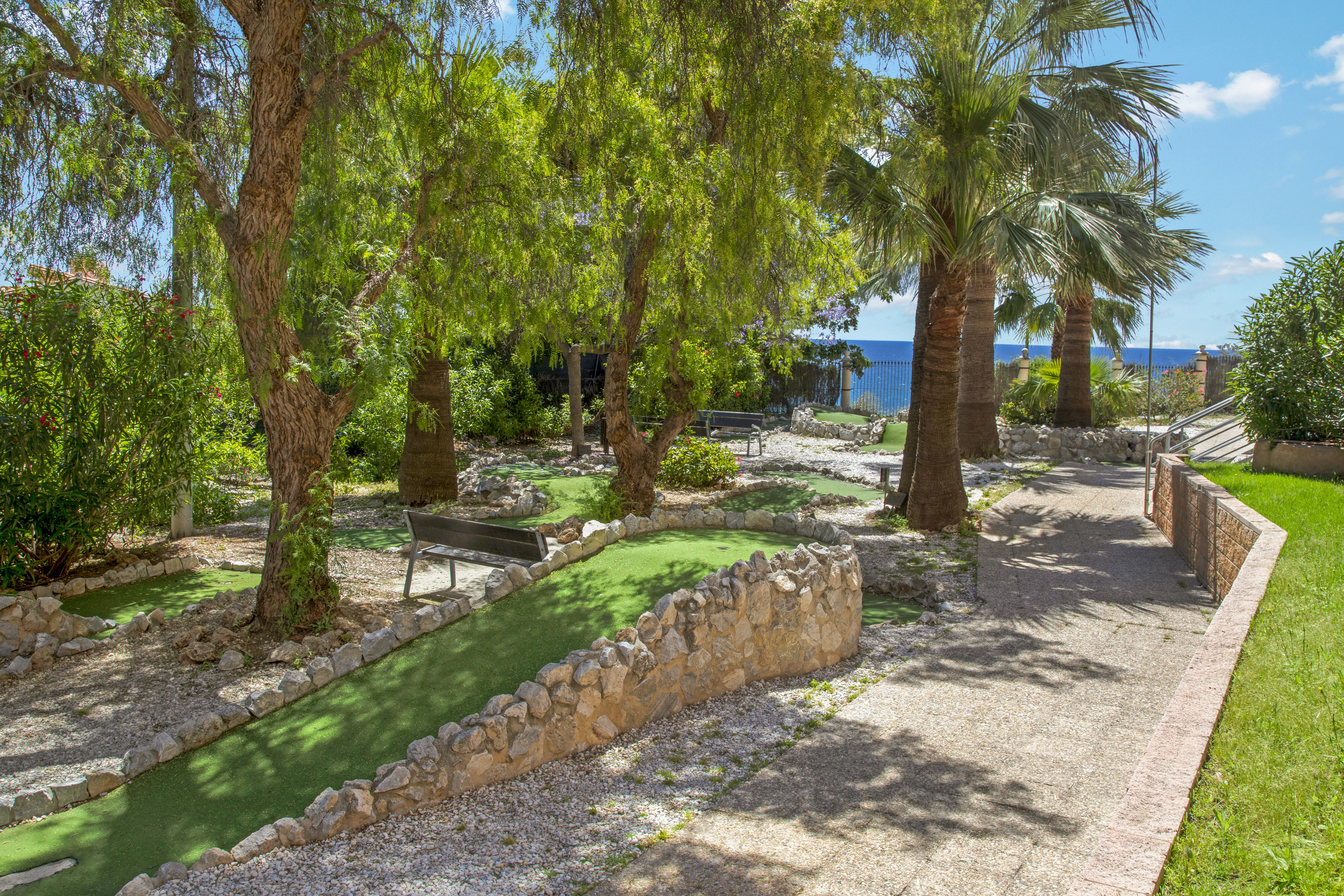 Mini golf course with green turf, palm trees, and a clear ocean view.