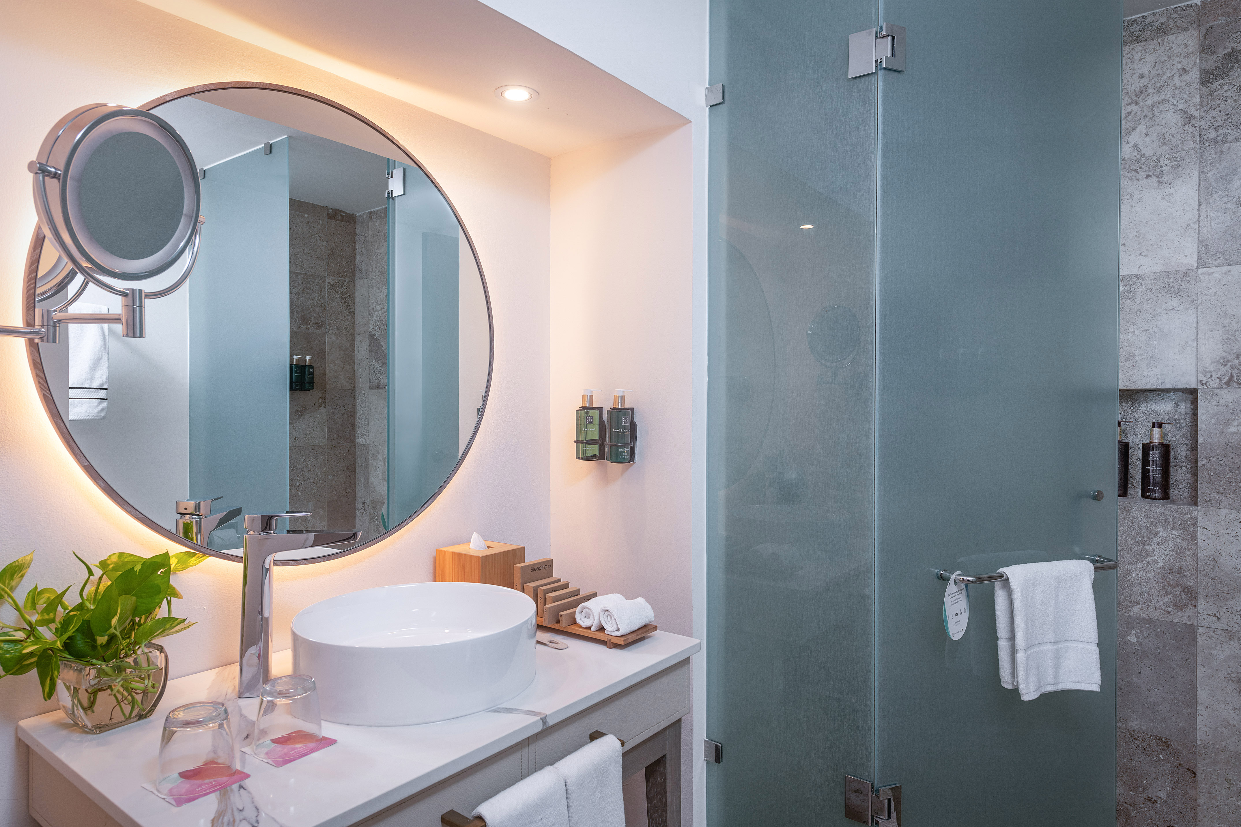 Modern bathroom with backlit mirror, vessel sink, and frosted glass shower.