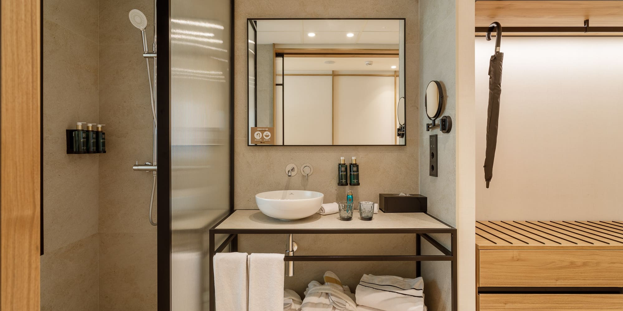 Modern hotel bathroom with glass shower, vessel sink, mirror, and towels.
