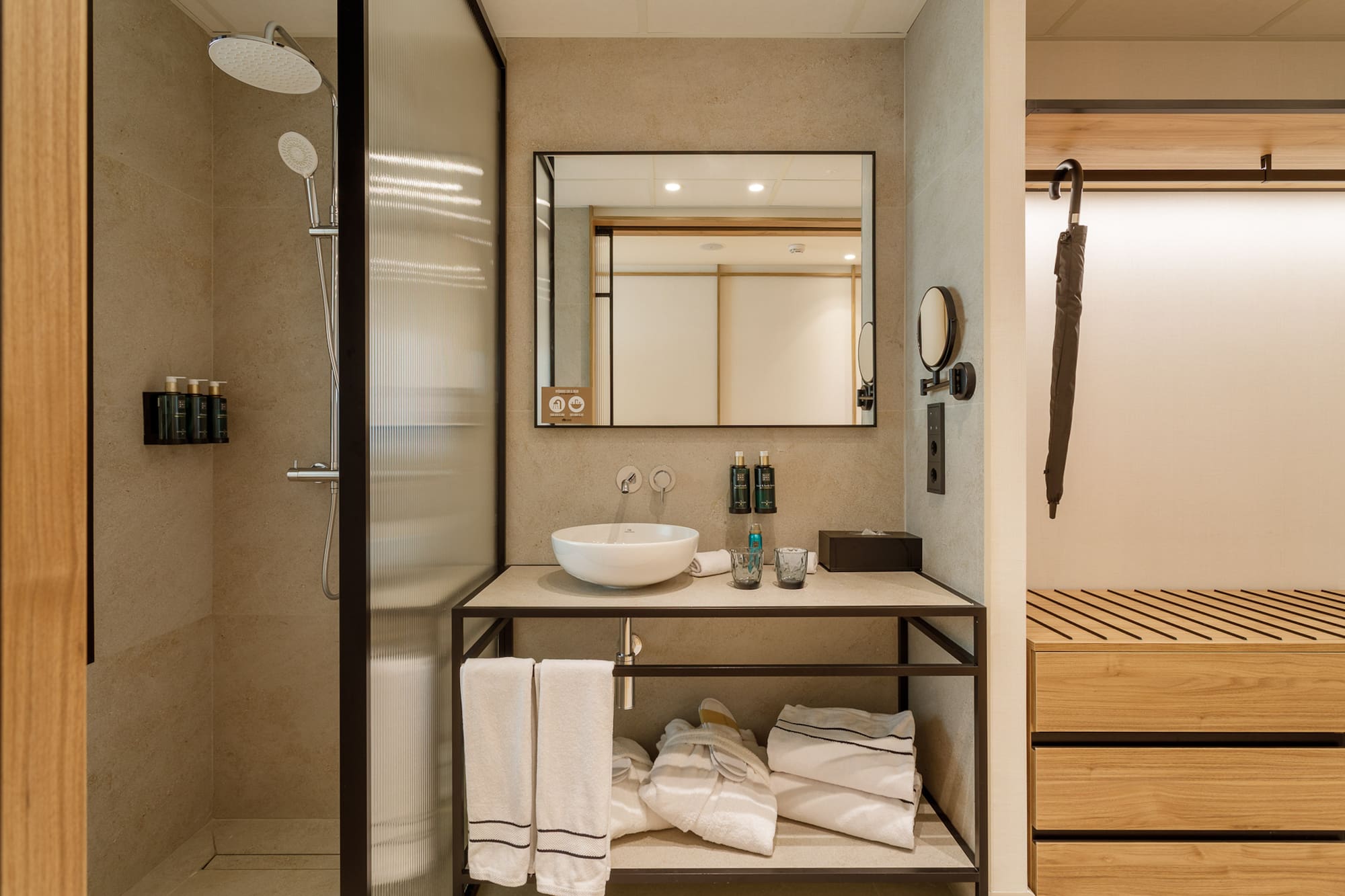 Modern hotel bathroom with glass shower, vessel sink, mirror, and towels.