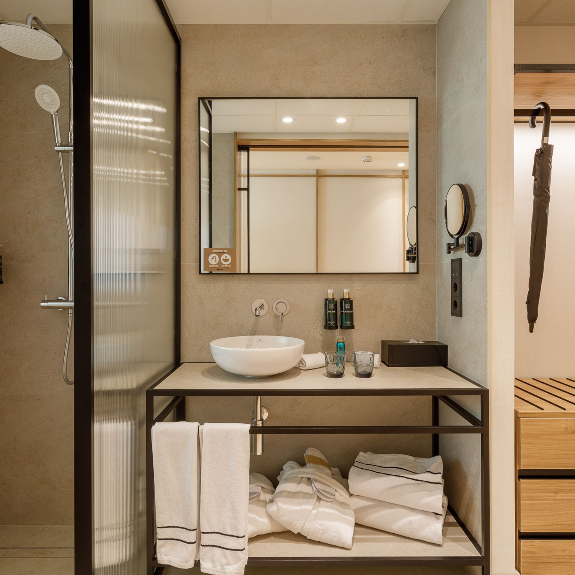 Modern hotel bathroom with glass shower, vessel sink, mirror, and towels.