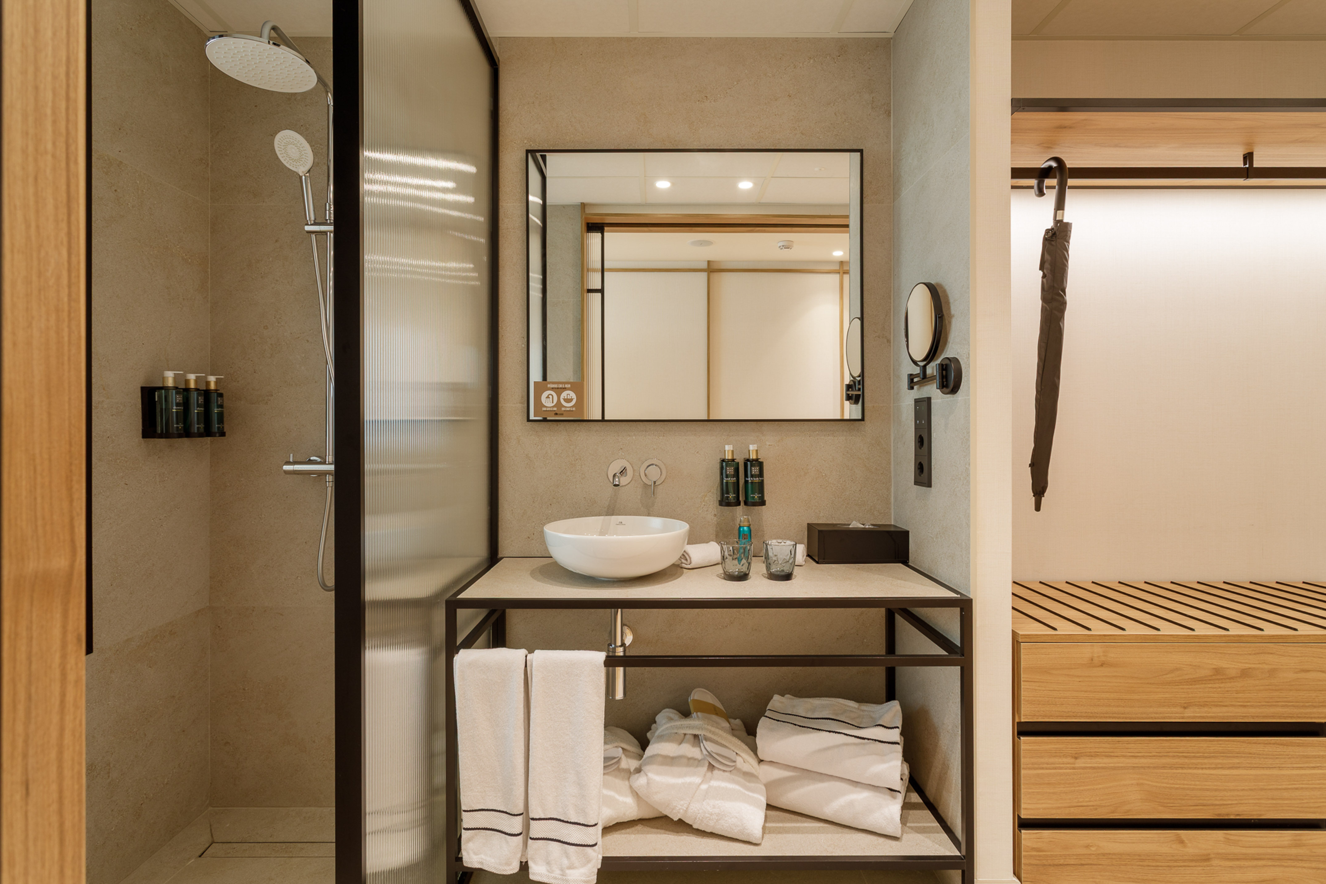 Neutral-toned hotel bathroom with glass shower, modern vanity, and closet storage.