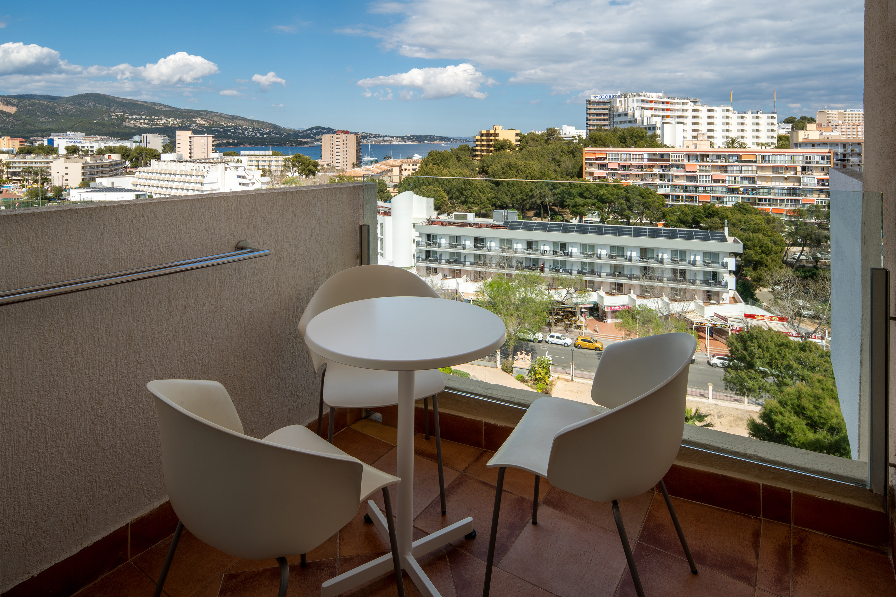 White table and chairs on balcony with coastal town, mountains, and sea view.