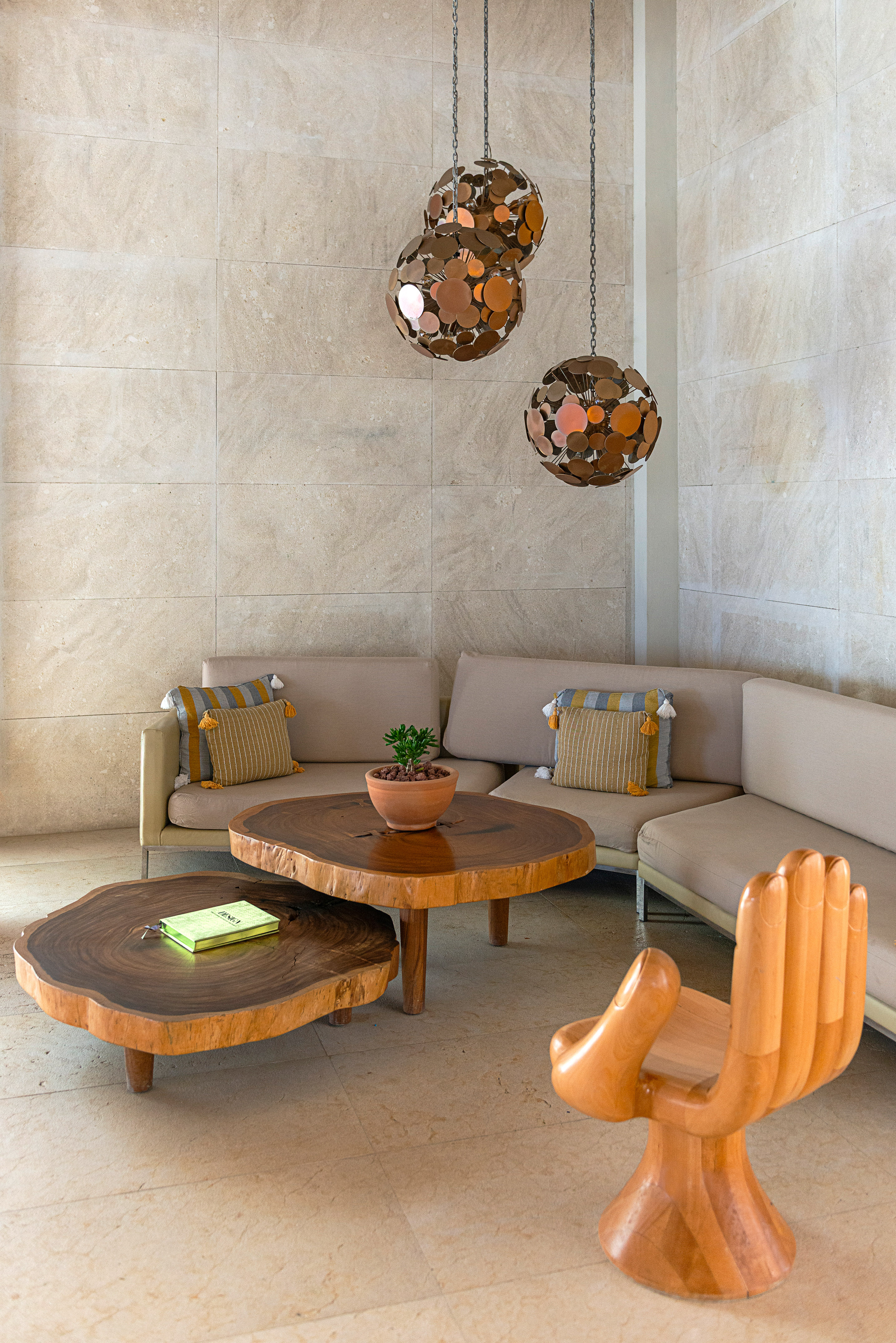 Lounge with live edge tables, beige sofa, wooden hand chair, and pendant lights.