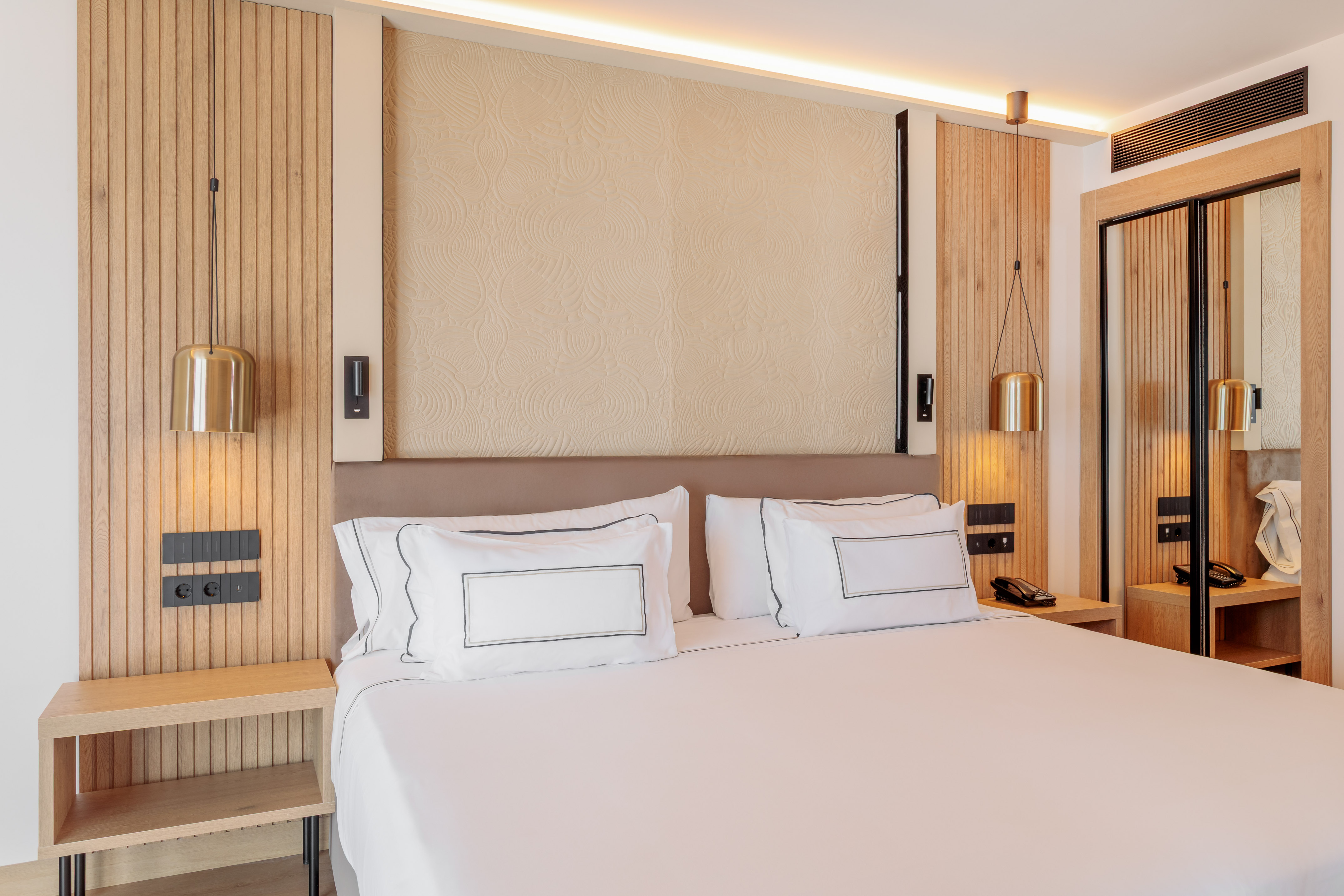 Modern hotel room with white bed, wood paneling, and golden pendant lights.