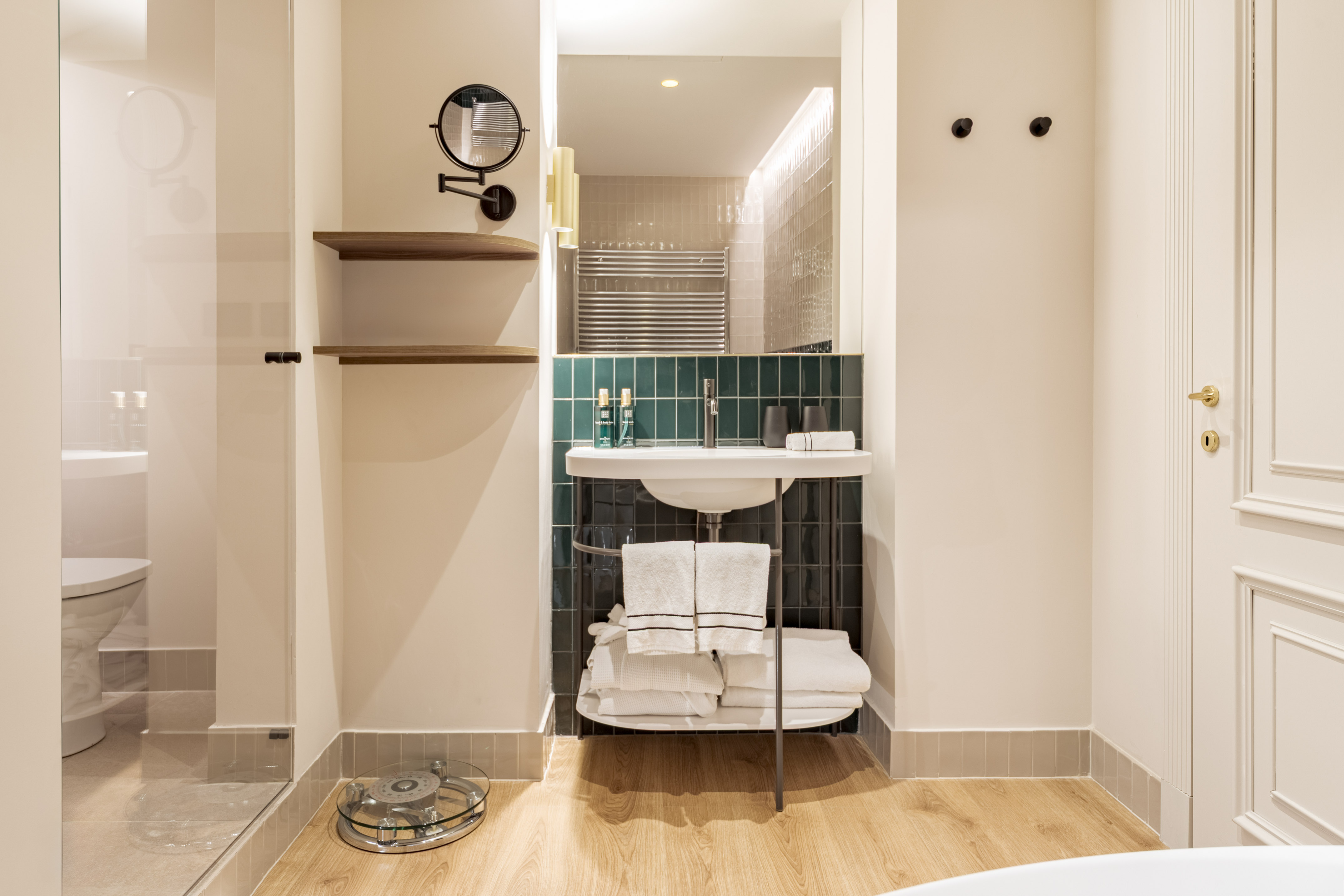 Modern bathroom with white vanity sink, dark green tiles, glass shower, wooden shelves.