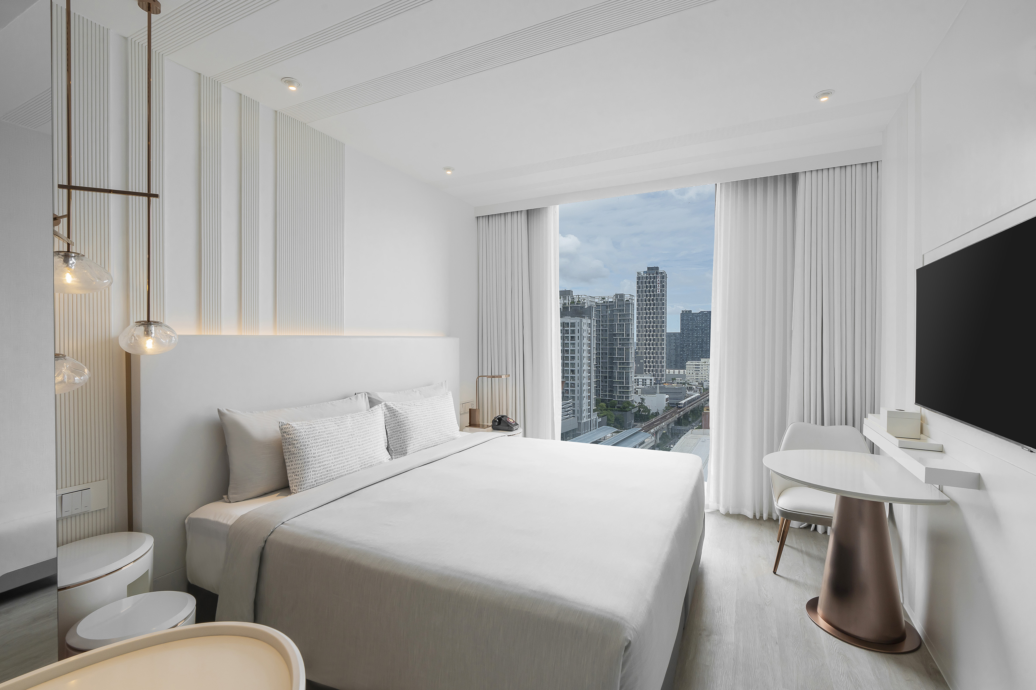 Contemporary hotel room with white bed, city view, and minimalist design.