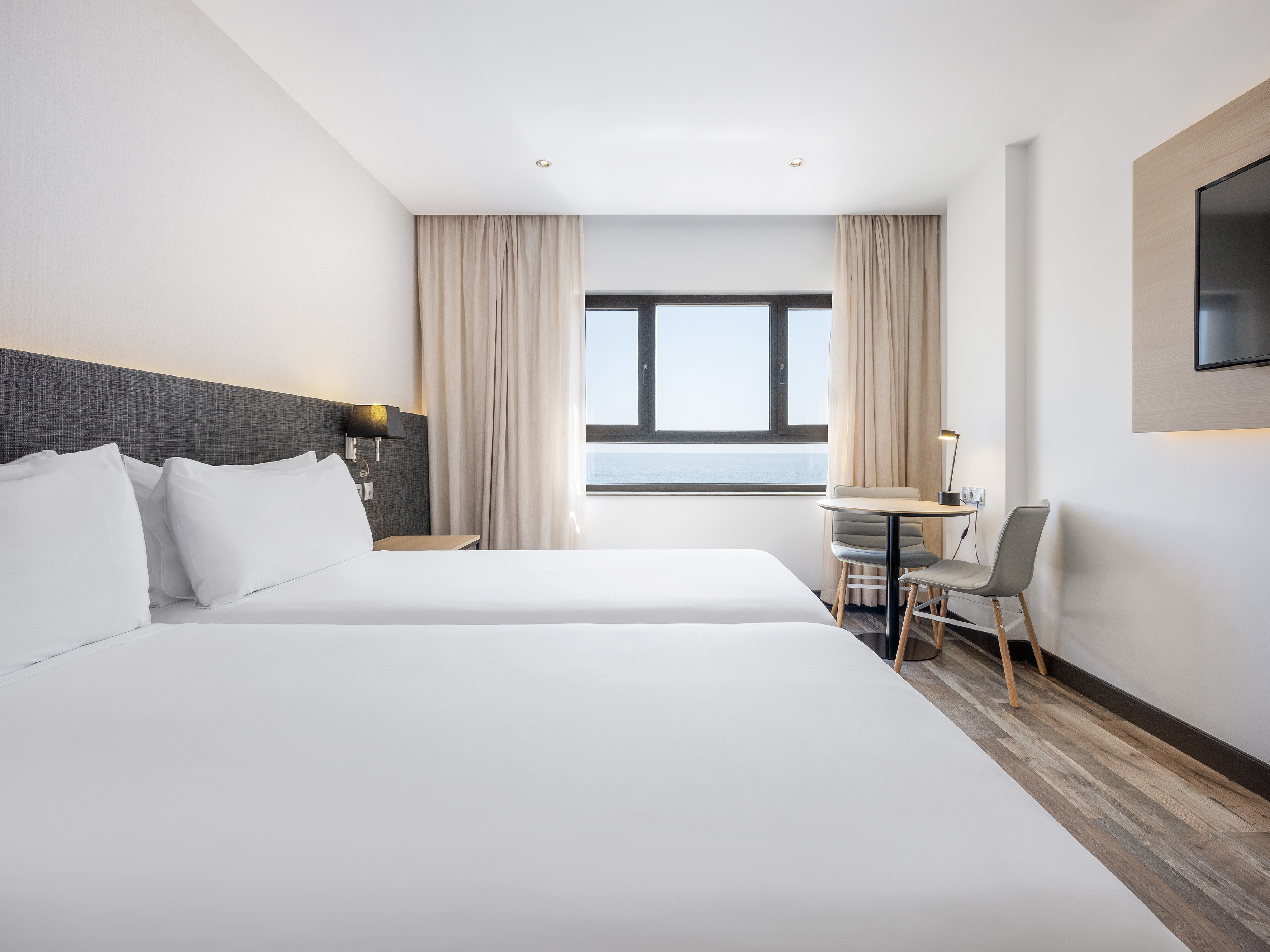 Hotel twin room with ocean view, white beds, and modern decor.