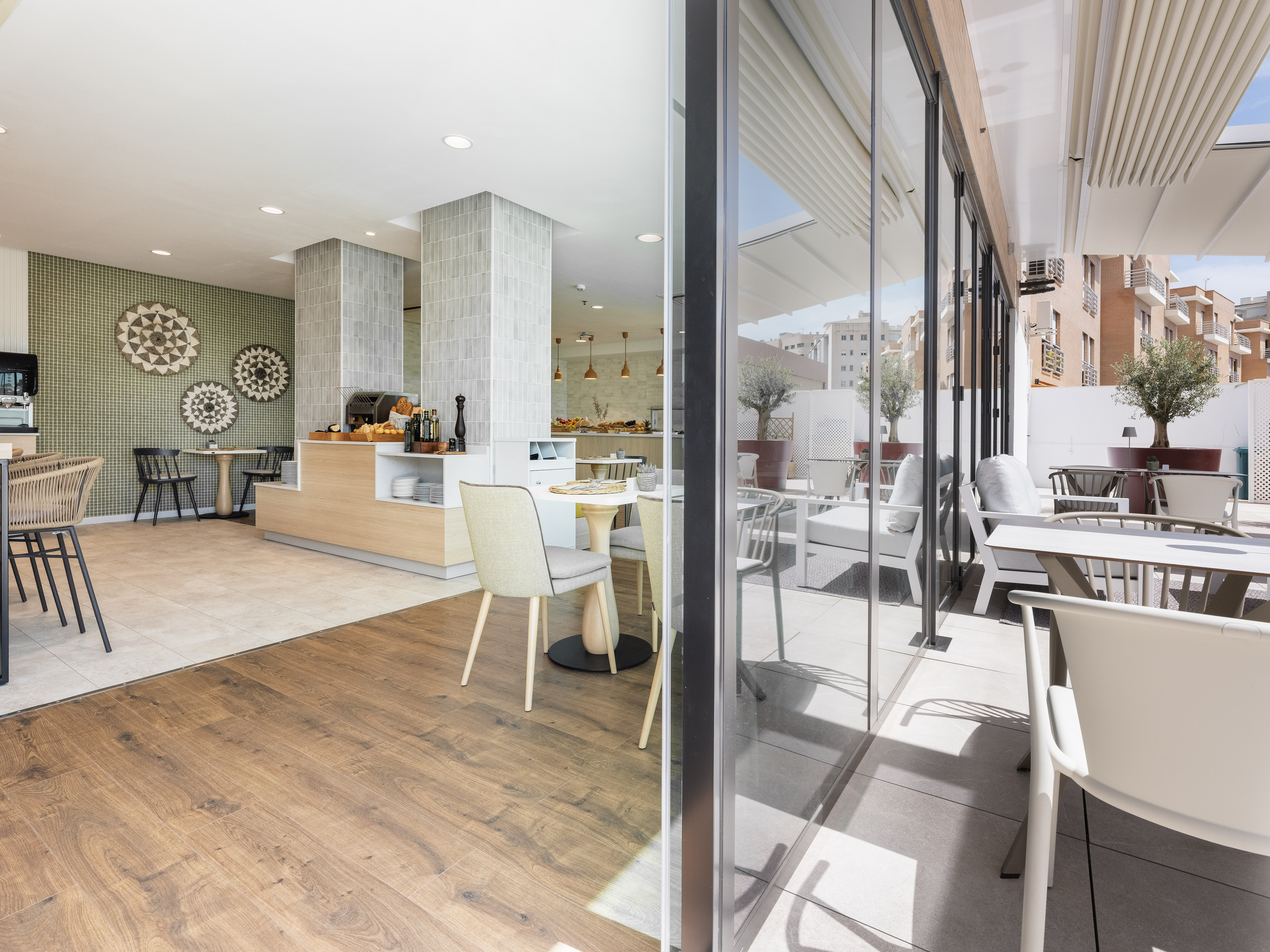 Modern indoor-outdoor hotel dining area with breakfast buffet and patio.