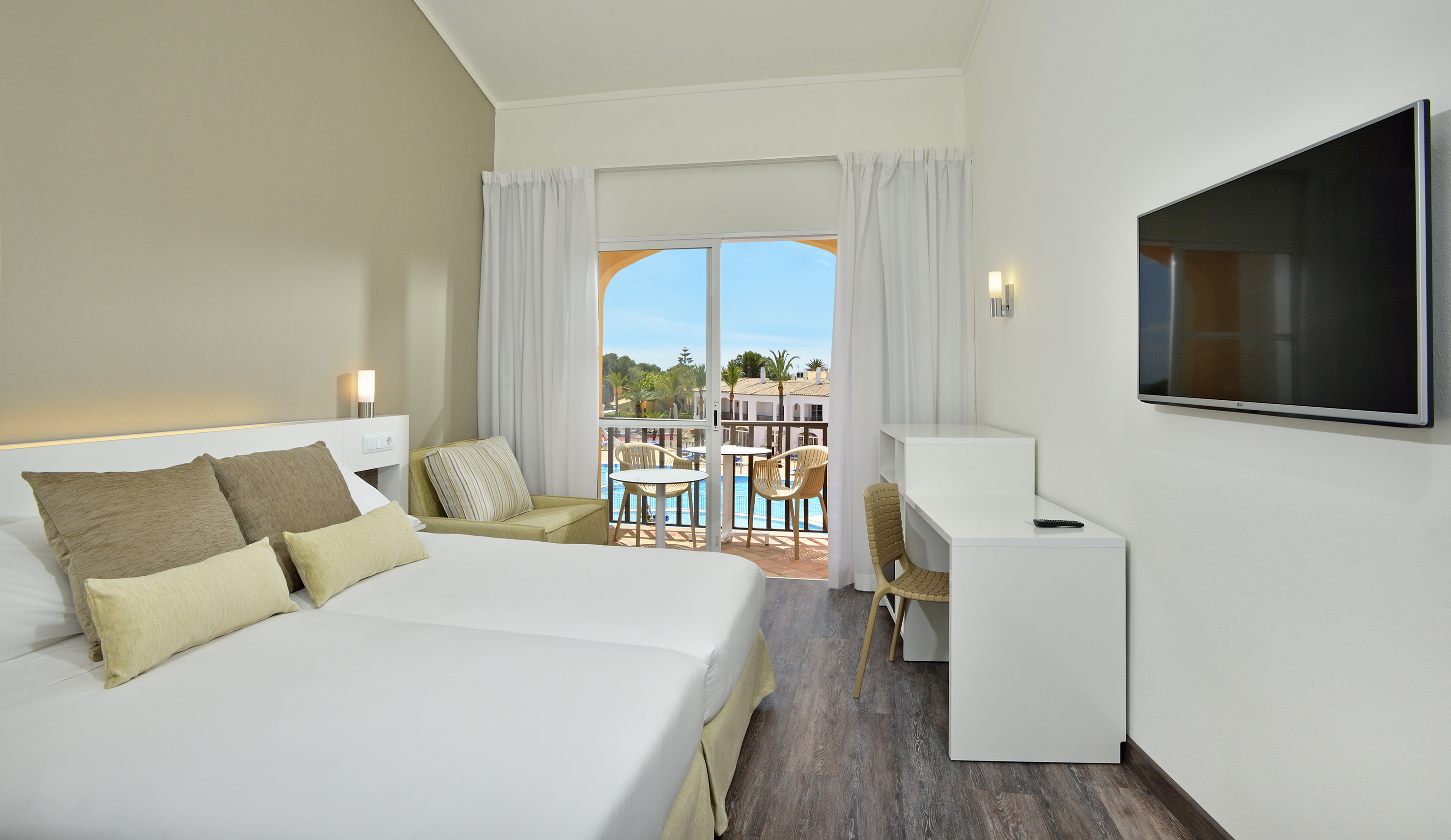 Modern hotel room with twin beds, balcony, and resort pool view.