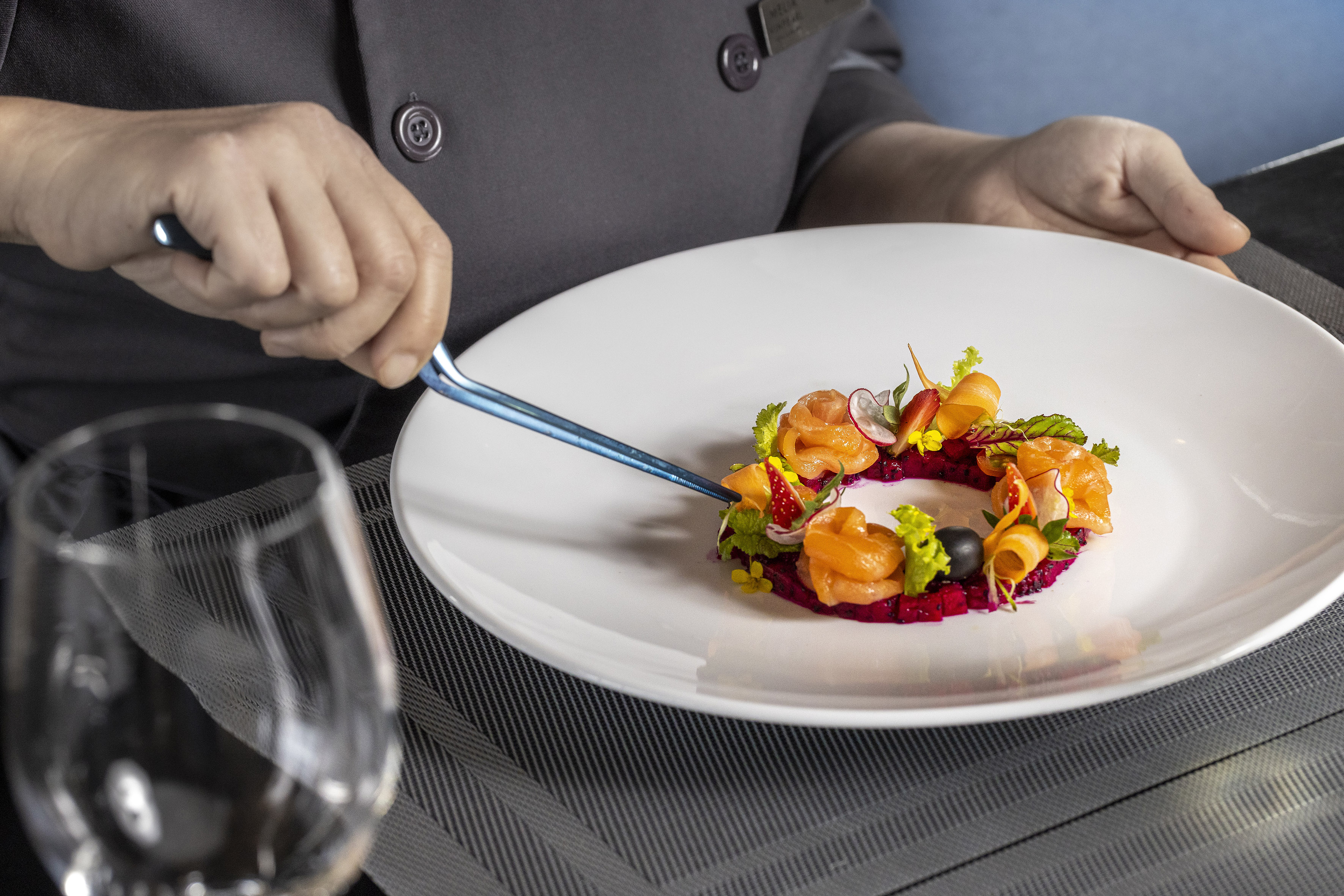 Chef plating gourmet salmon and vegetable appetizer with tweezers.