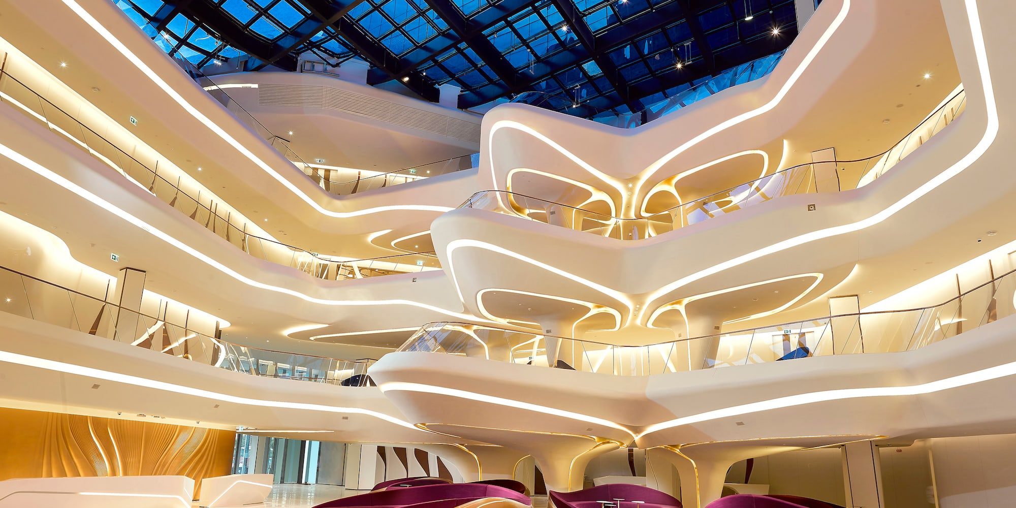 Modern atrium with curved design, glass roof, and purple lounge seating.