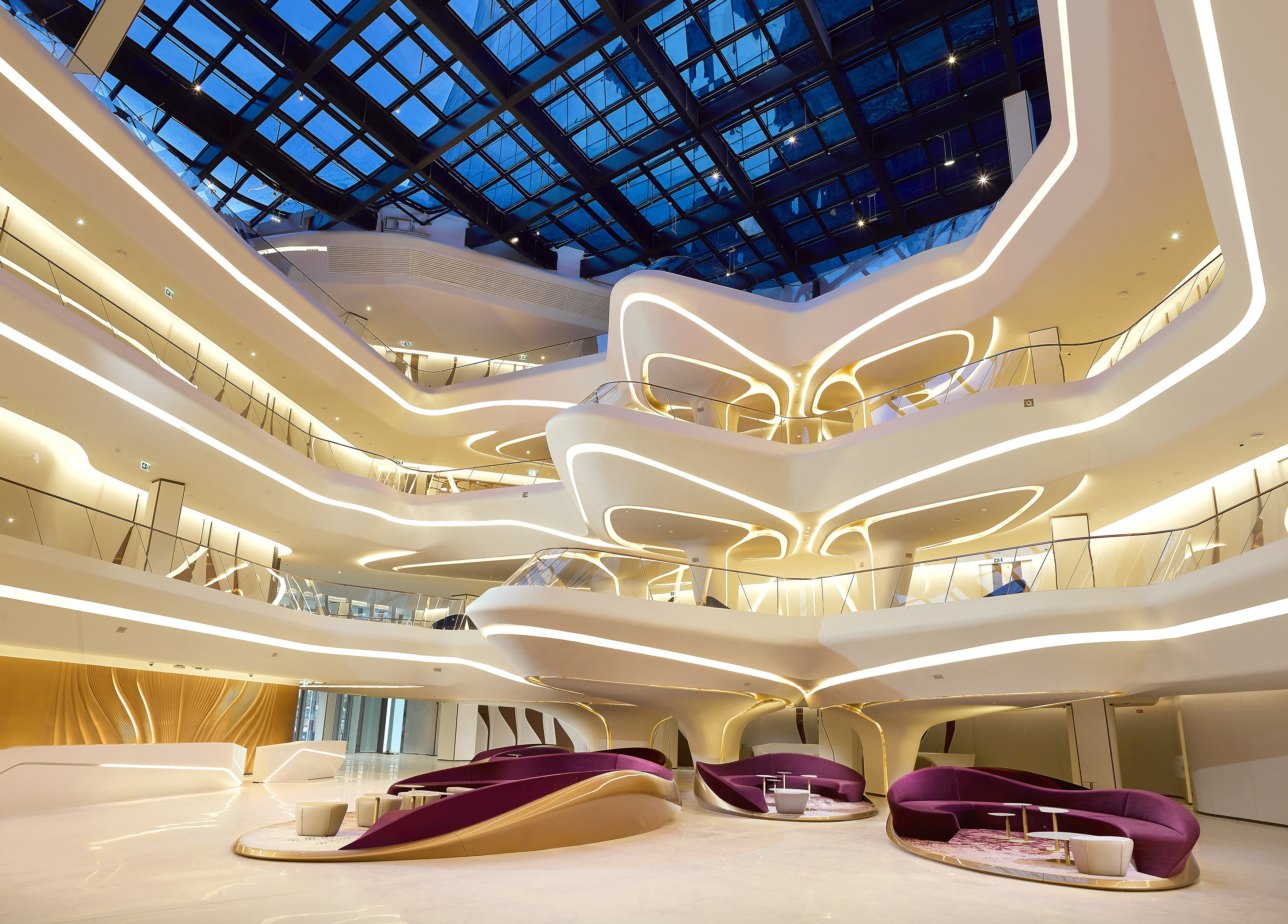 Futuristic atrium with glowing curved levels, glass roof, and luxury seating.