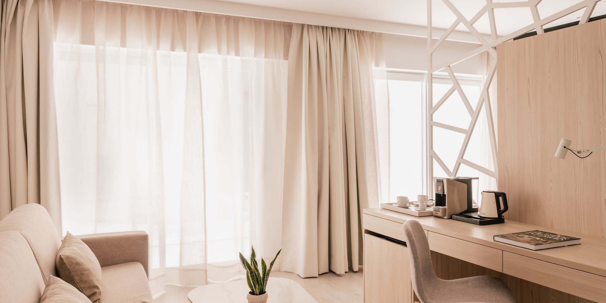 Modern hotel room with sofa, light wood desk, and bright neutral decor.