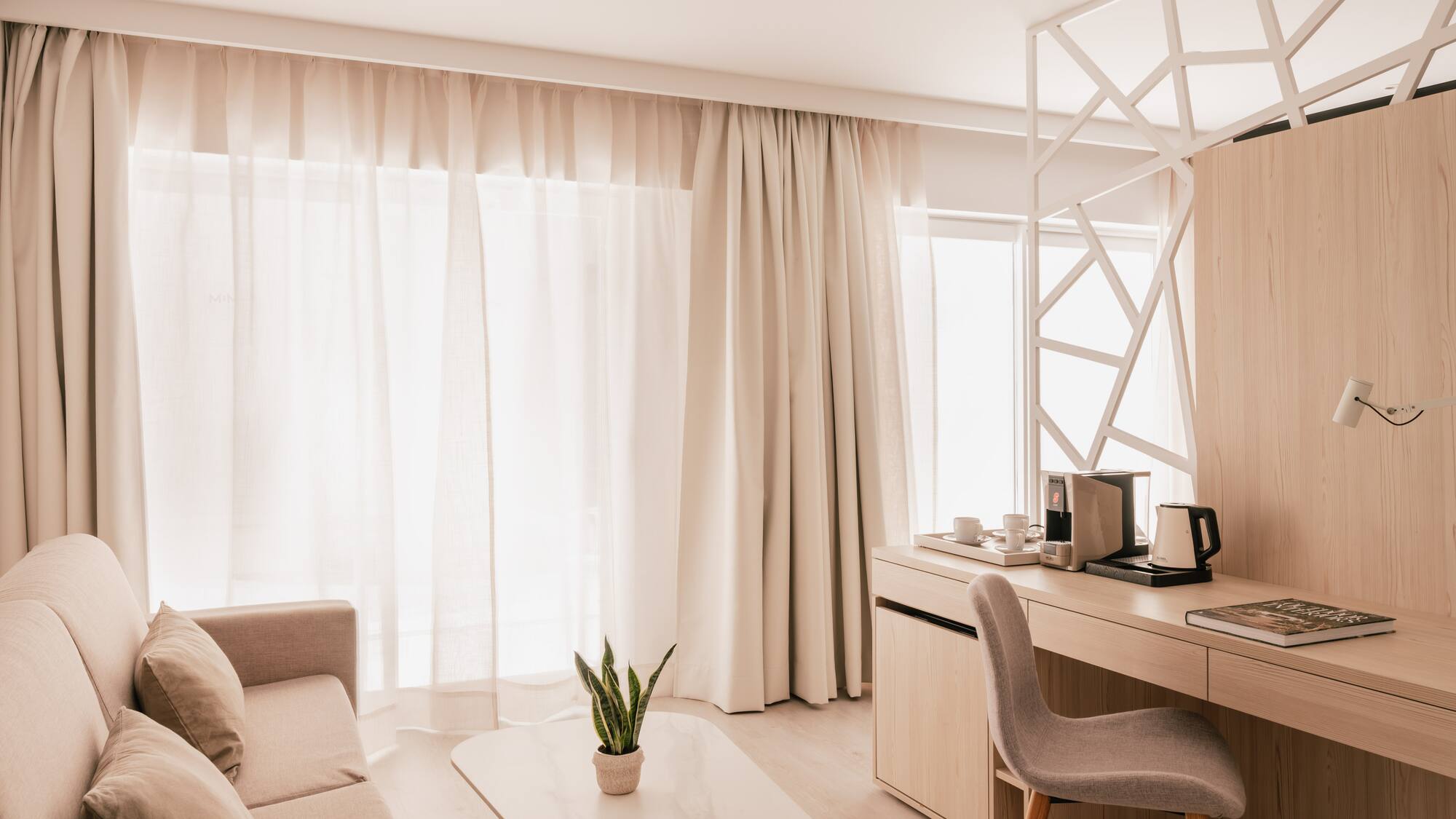 Modern hotel room with sofa, light wood desk, and bright neutral decor.