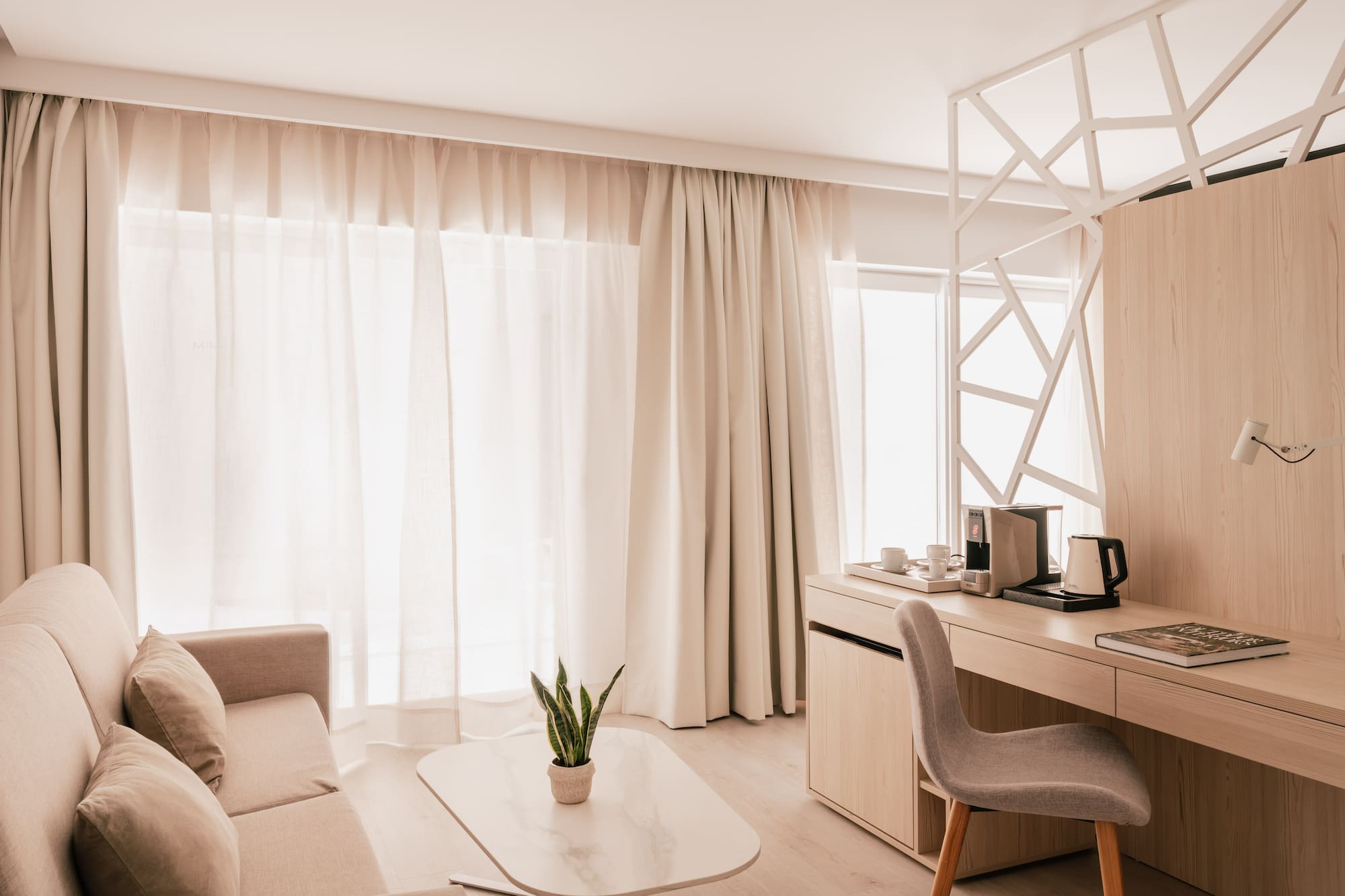 Modern hotel room with sofa, light wood desk, and bright neutral decor.