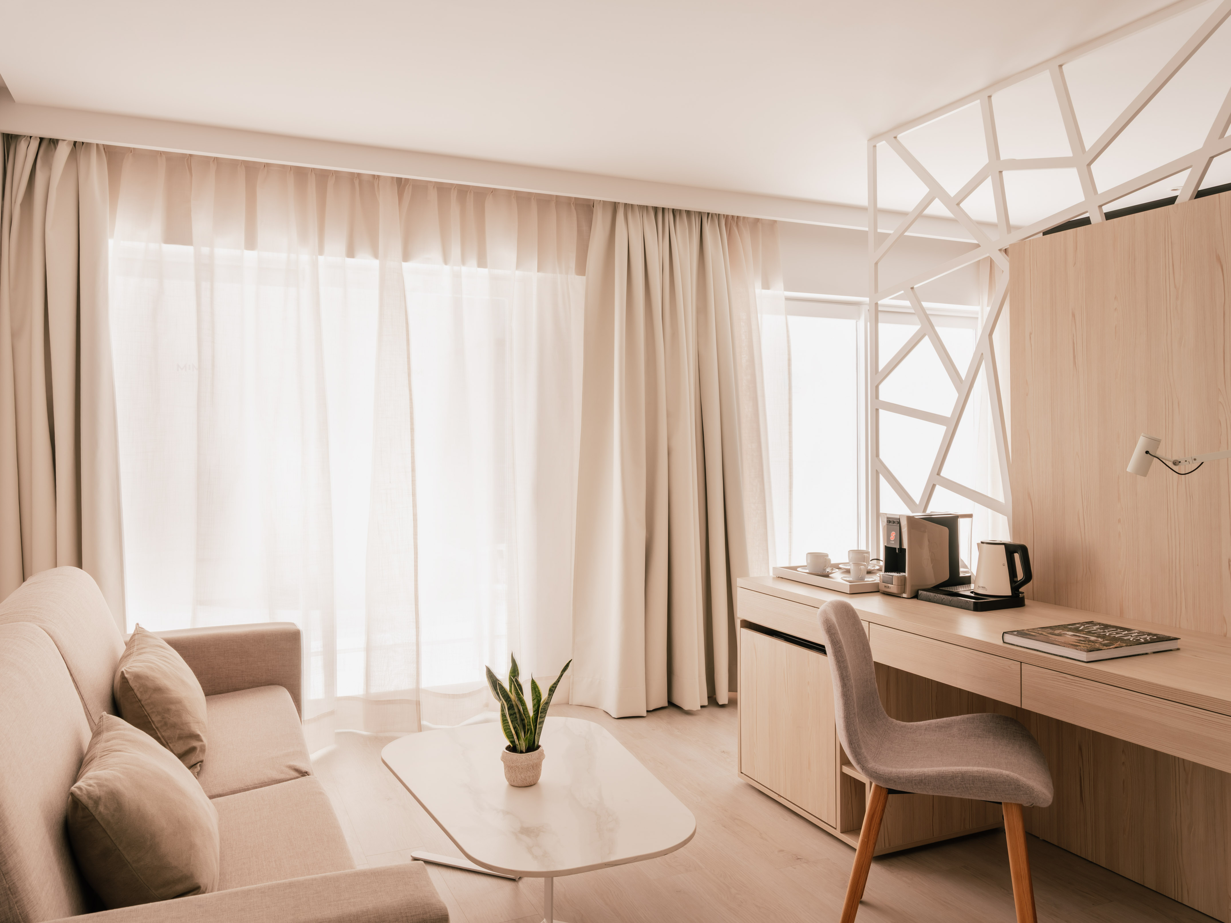 Modern hotel room with sofa, light wood desk, and bright neutral decor.