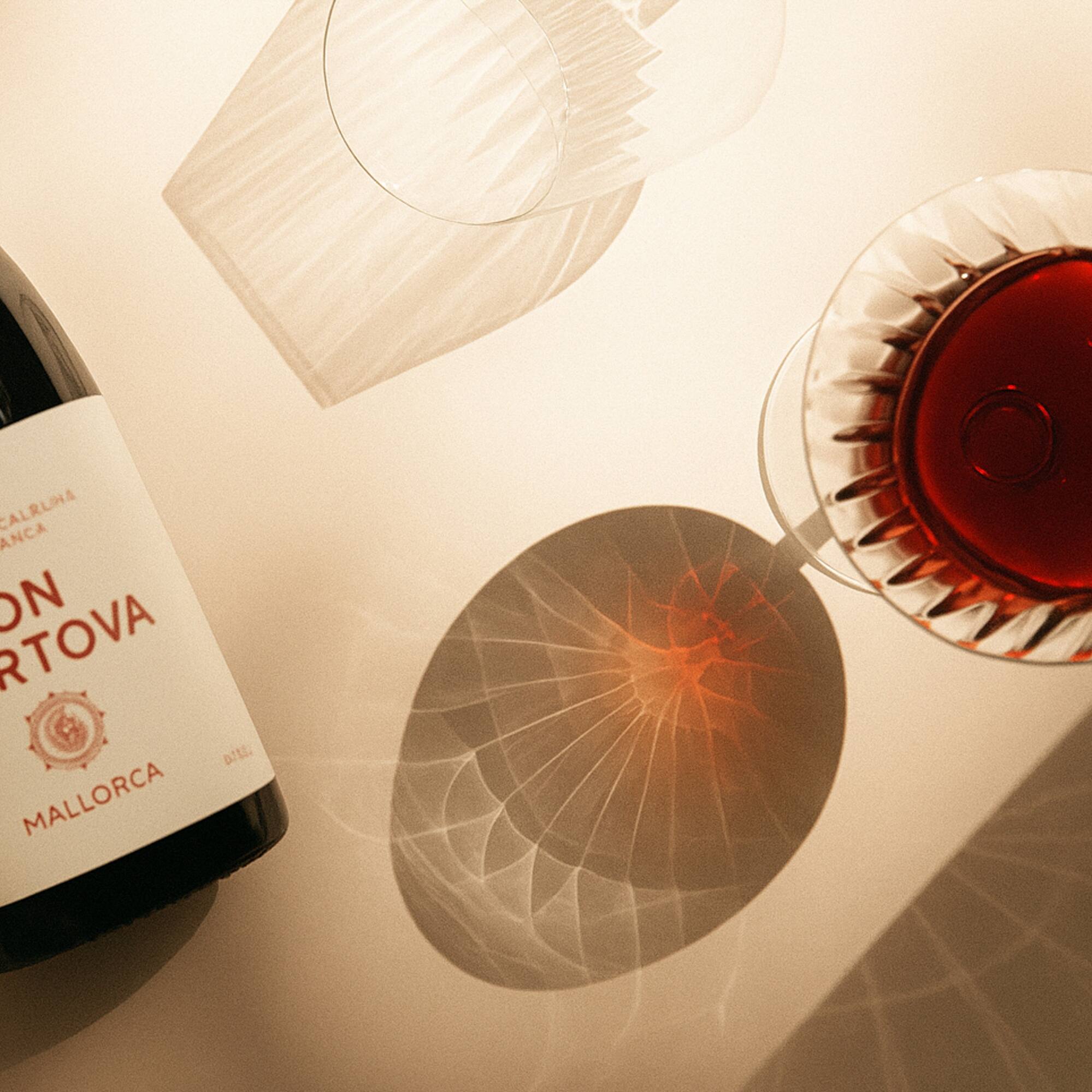 Mallorca red wine bottle, glass of wine, empty glass, sunlit shadows.