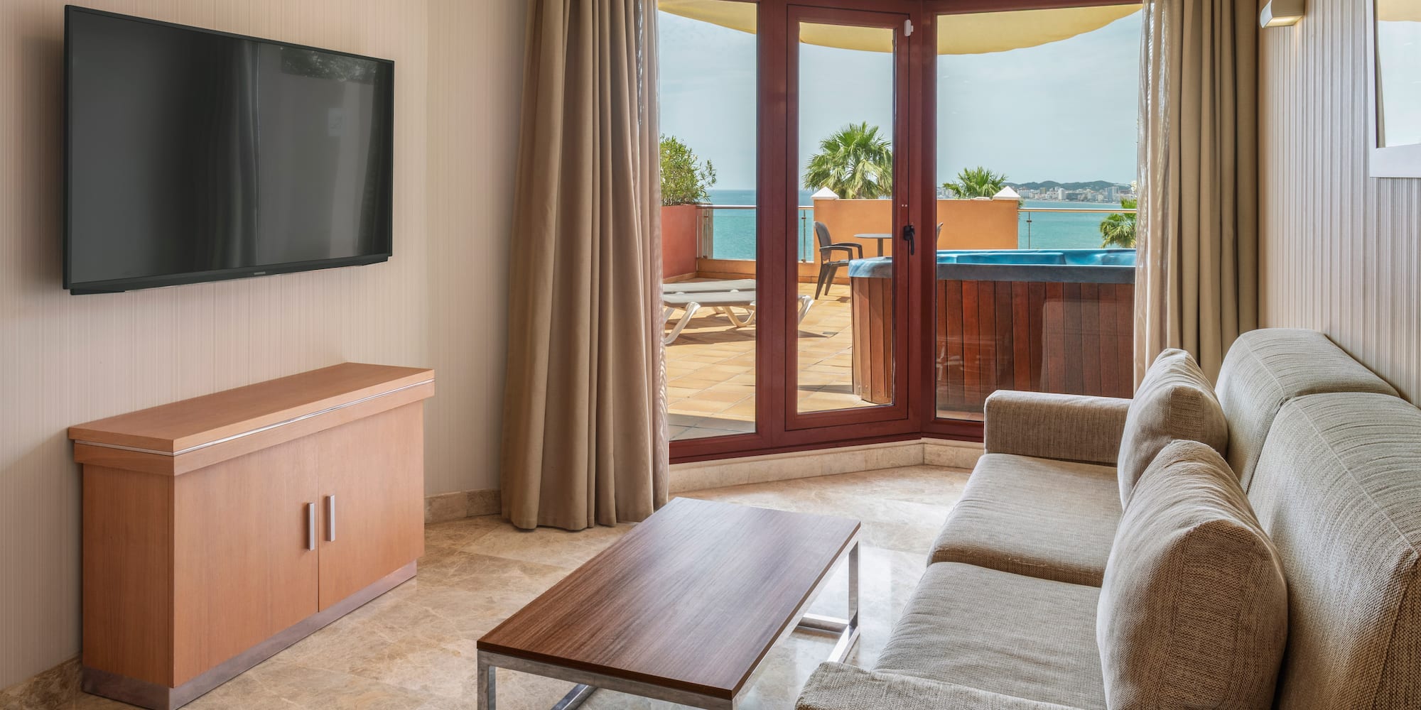 Hotel living room with sea view balcony, hot tub, sofa, and TV.