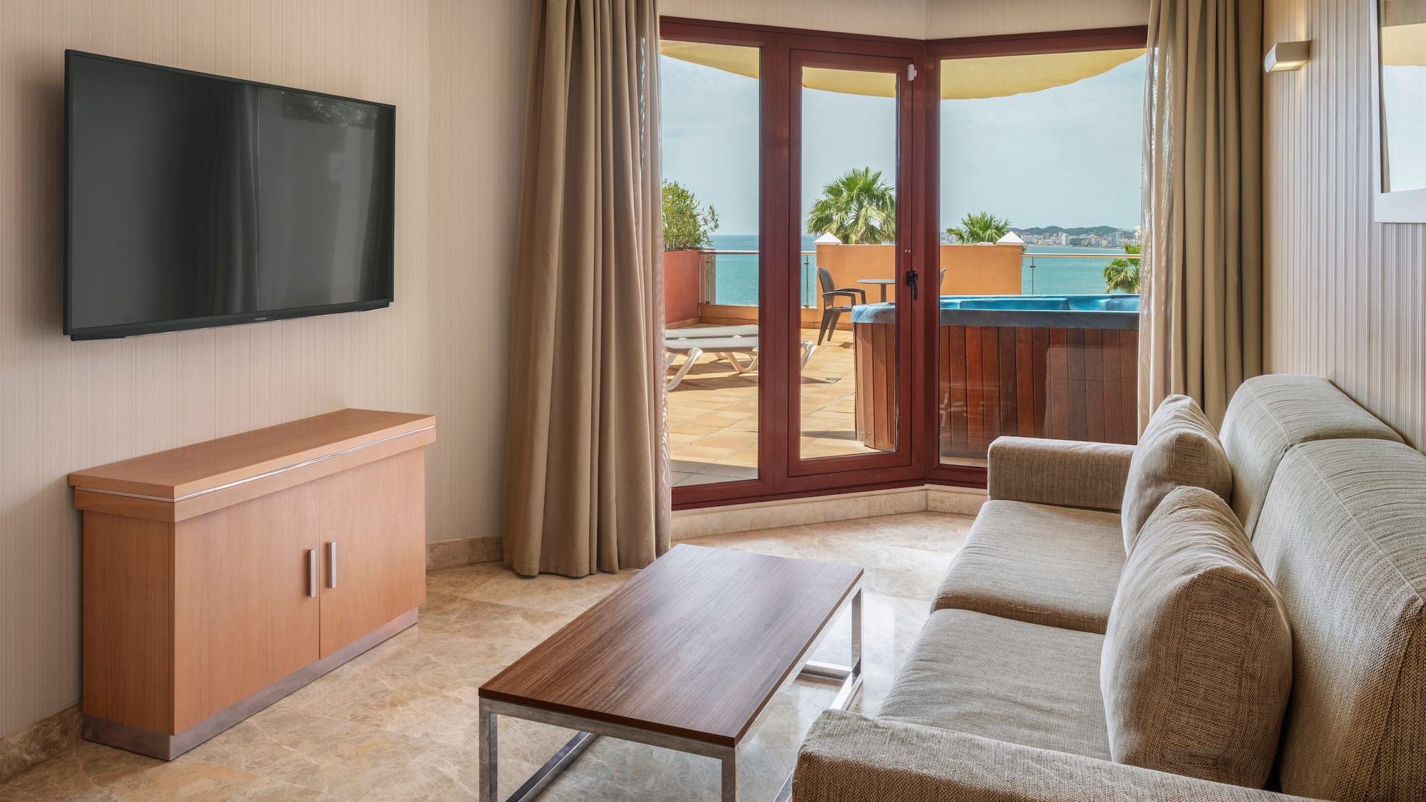 Hotel living room with sea view balcony, hot tub, sofa, and TV.