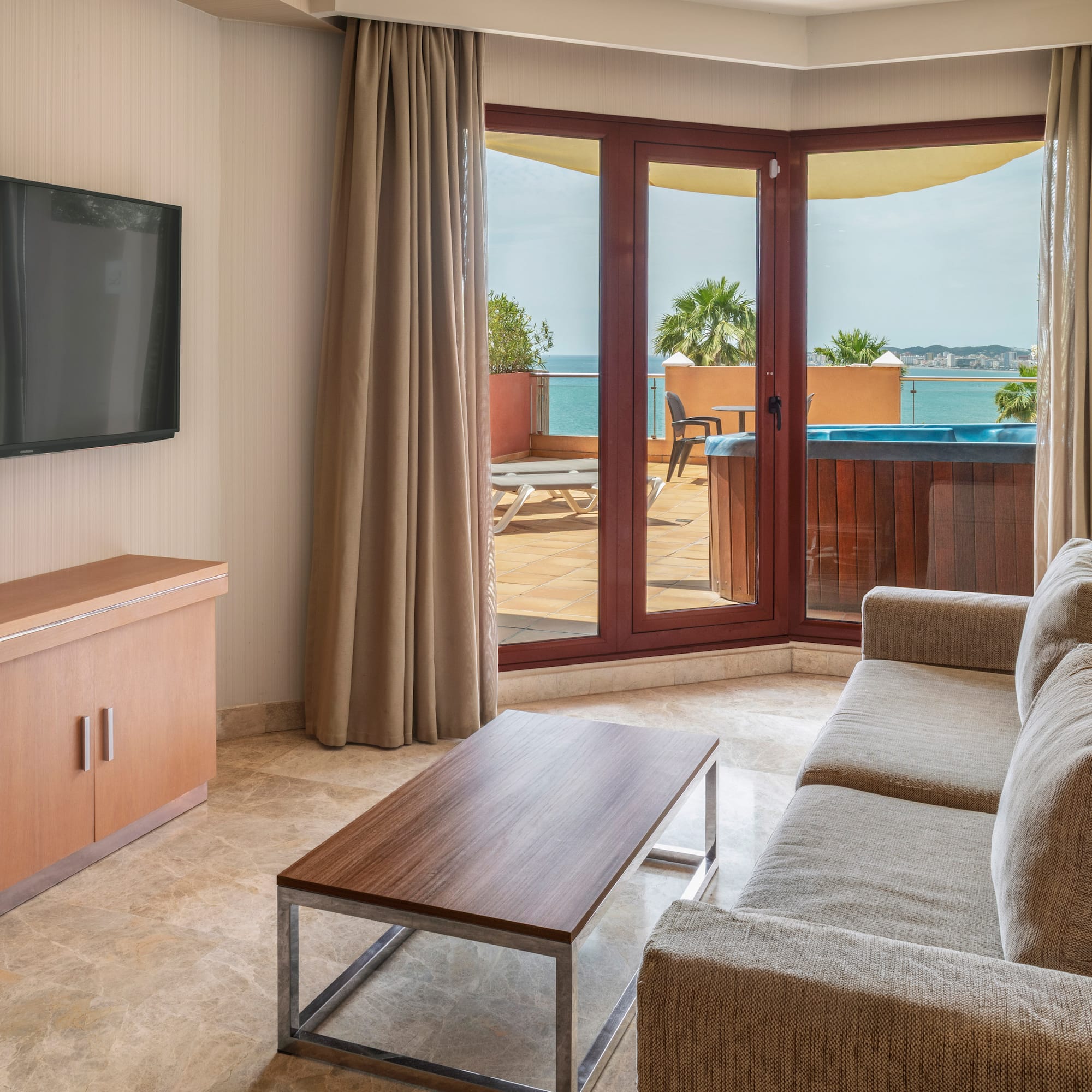 Hotel living room with sea view balcony, hot tub, sofa, and TV.