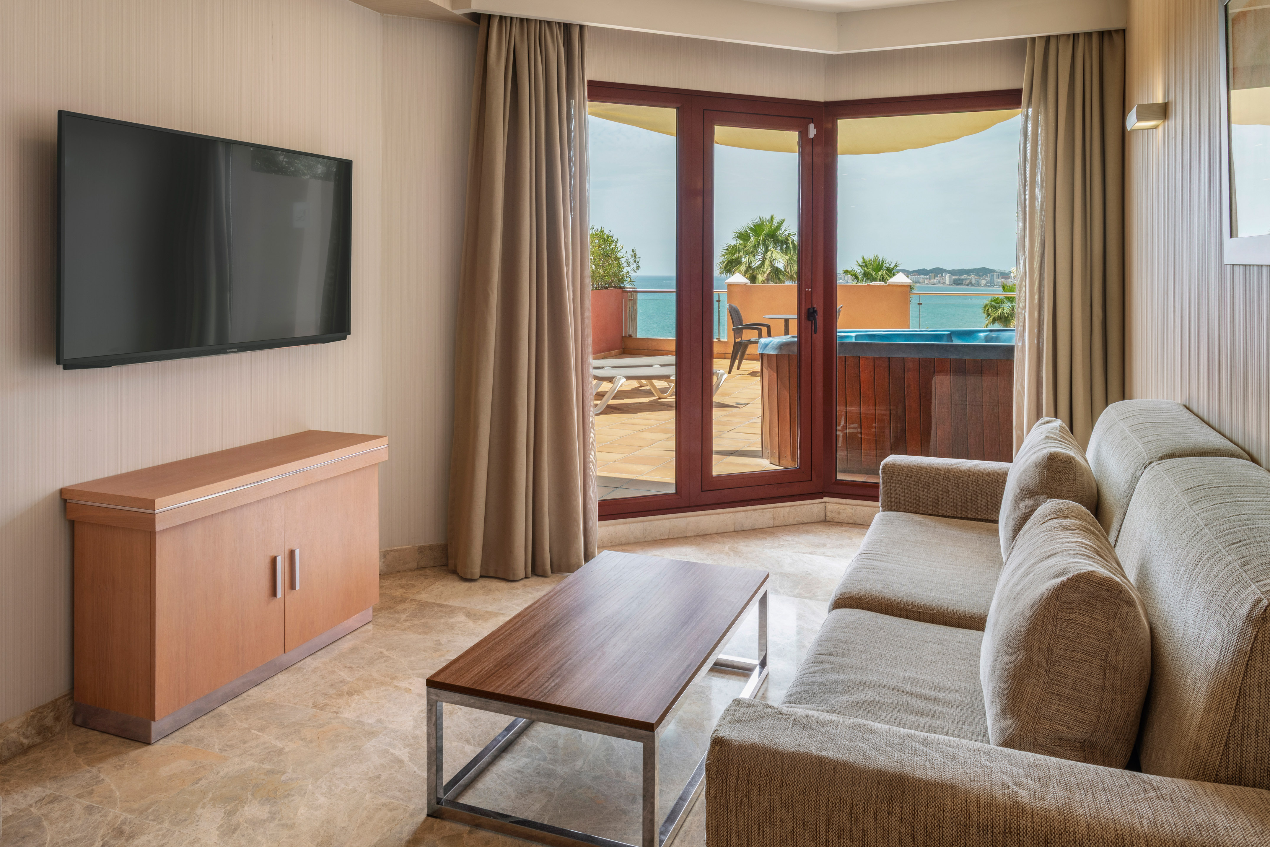 Hotel living room with sea view balcony, hot tub, sofa, and TV.