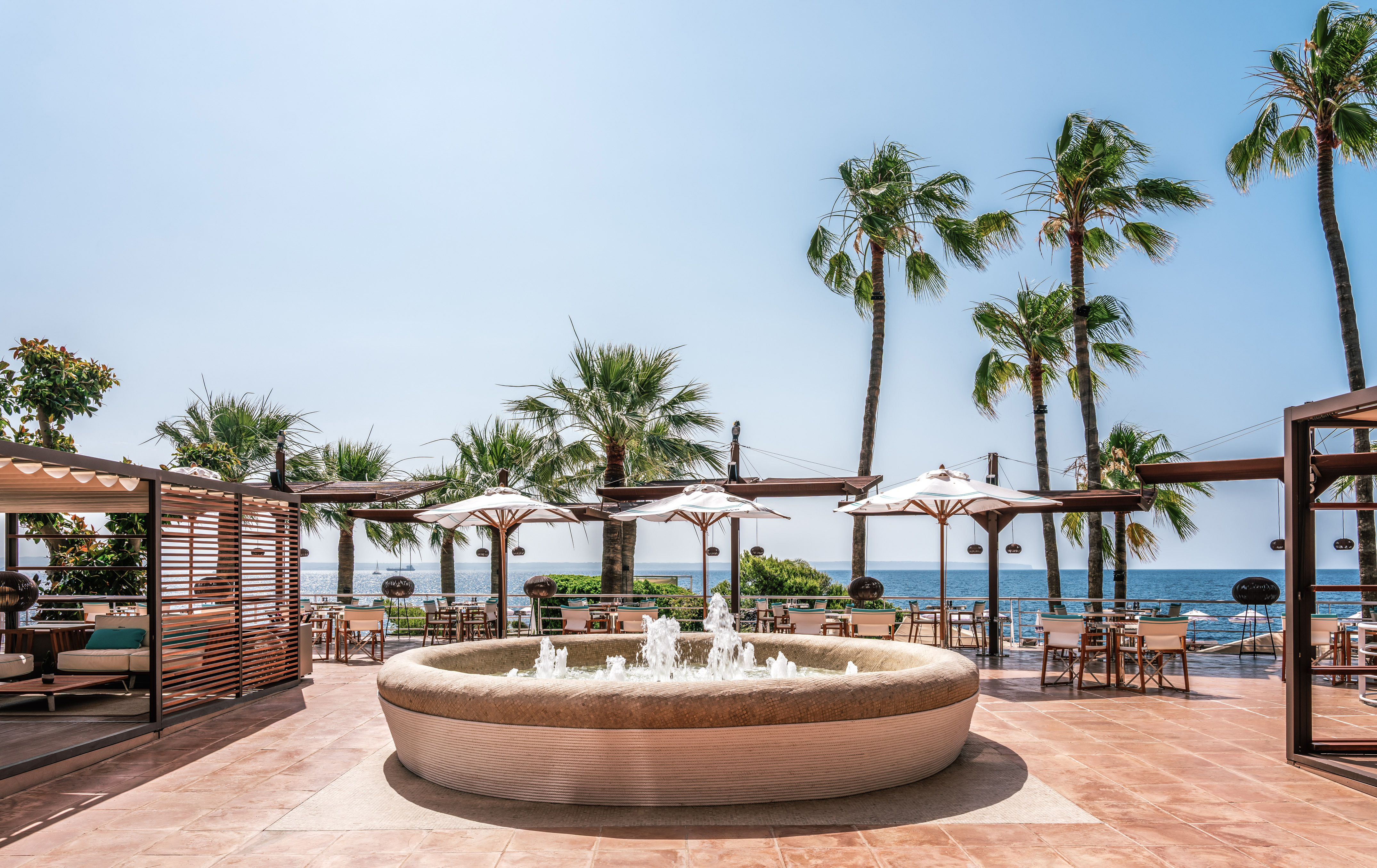 Oceanfront resort patio with fountain, palm trees, and outdoor seating.