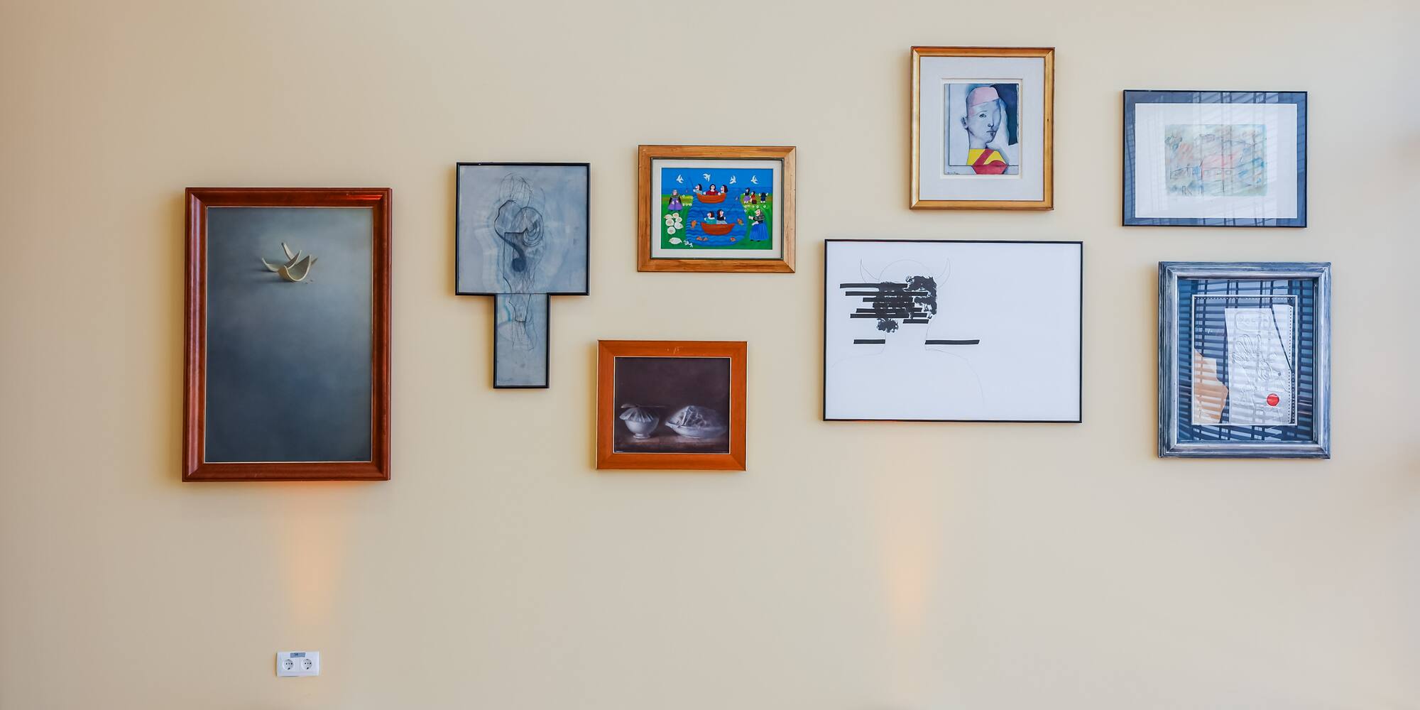 Gallery wall with diverse framed art, spotlighted on a cream-colored wall.