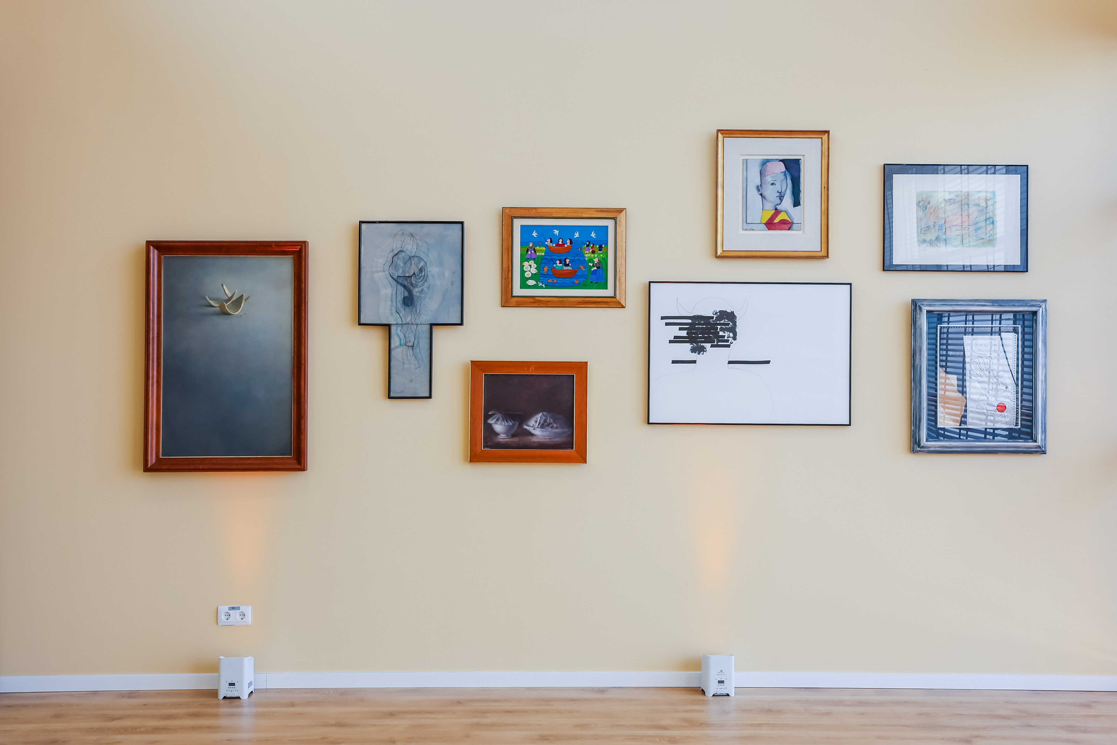 Gallery wall with diverse framed art, spotlighted on a cream-colored wall.