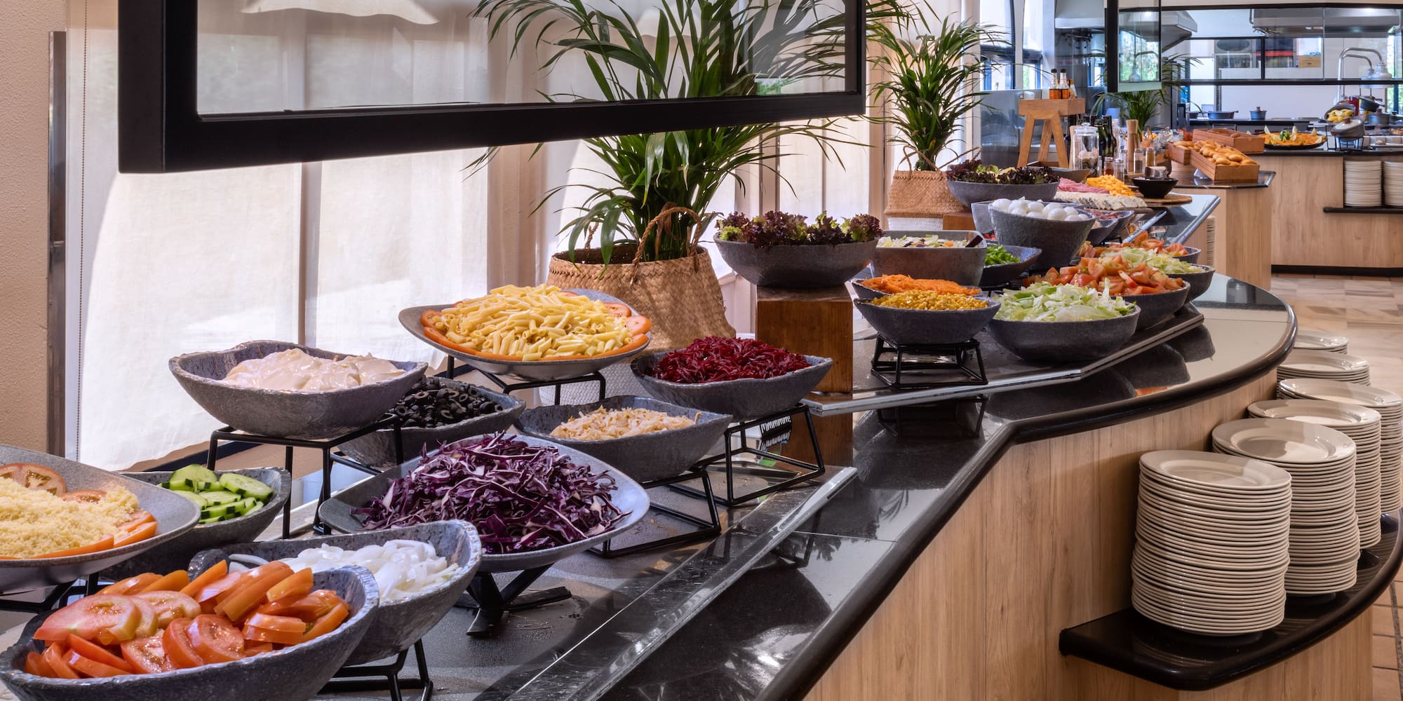 Fresh salad buffet with vegetables, pasta, and toppings in a bright restaurant.
