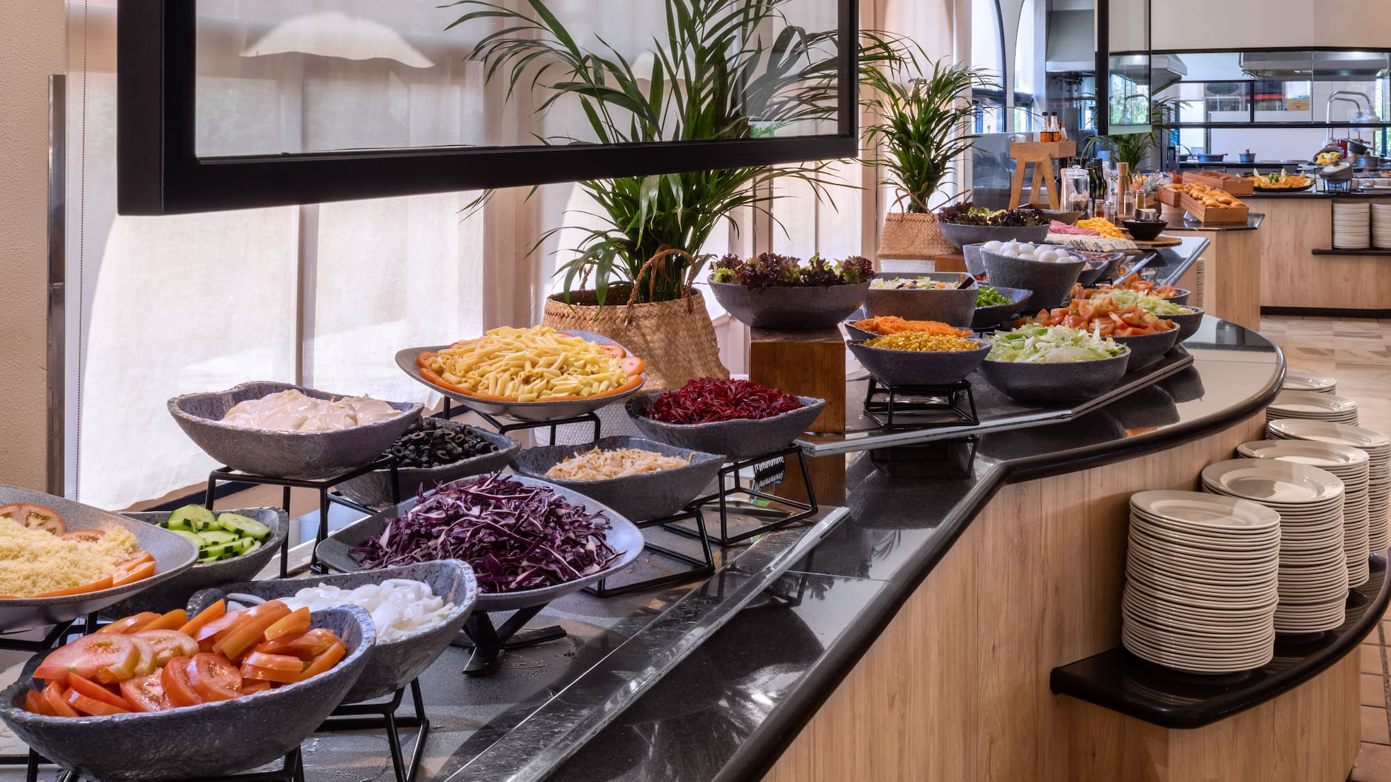 Fresh salad buffet with vegetables, pasta, and toppings in a bright restaurant.