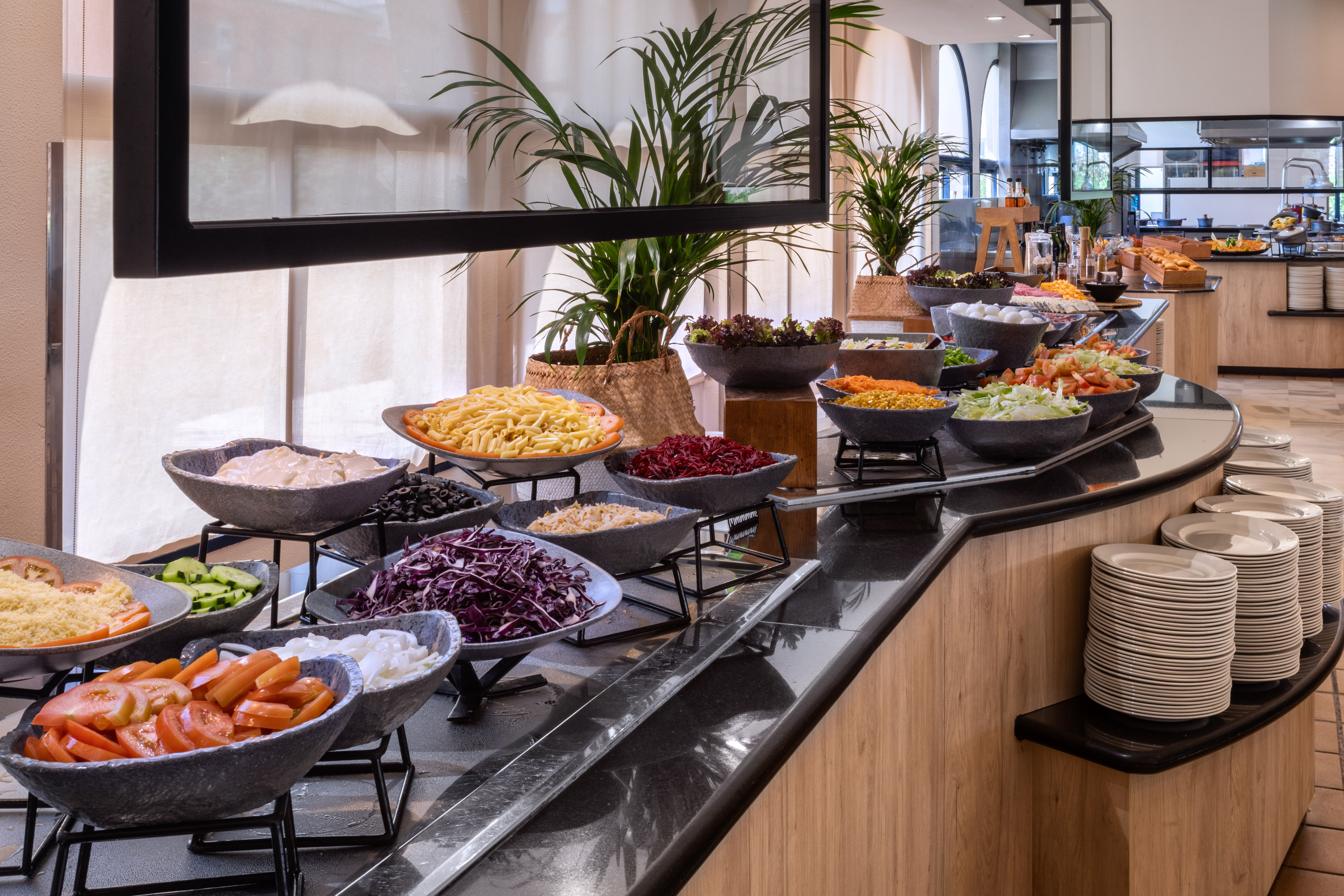 Fresh salad buffet with vegetables, pasta, and toppings in a bright restaurant.