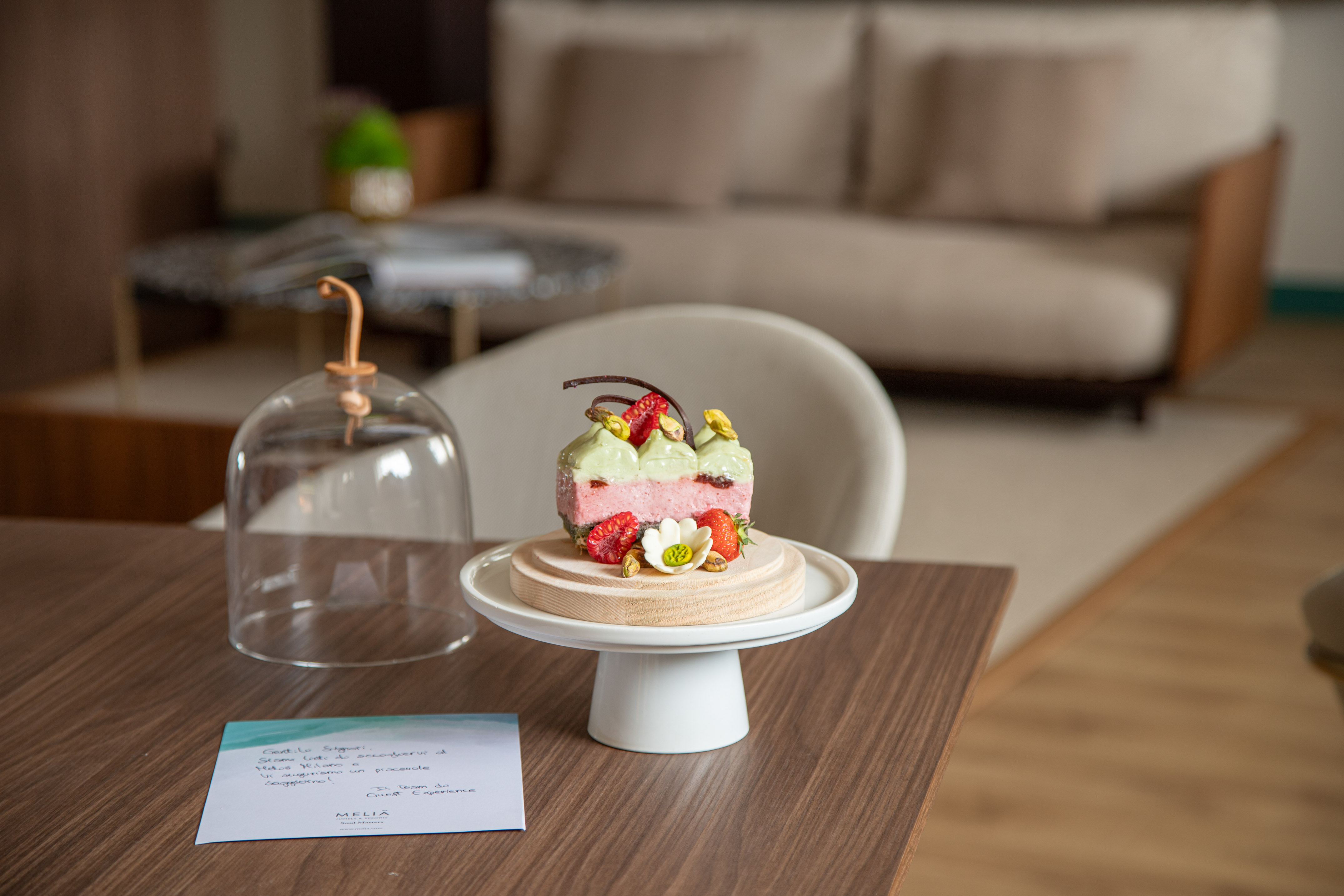 Luxury strawberry pistachio cake and welcome note in a modern hotel room.