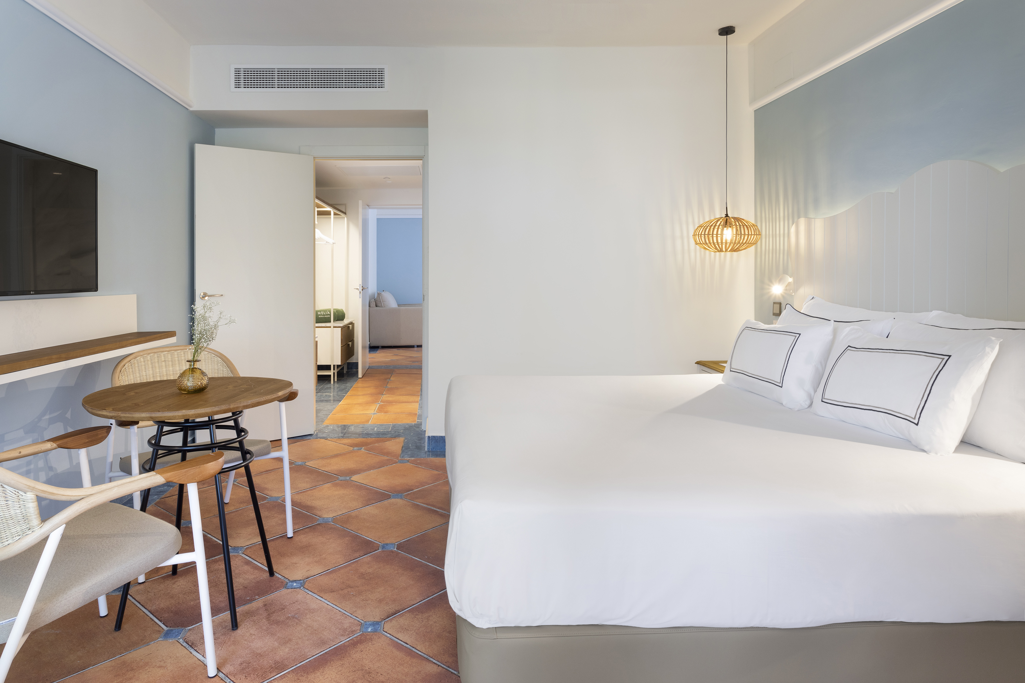 Mediterranean hotel suite with king bed, dining set, and terracotta floors.