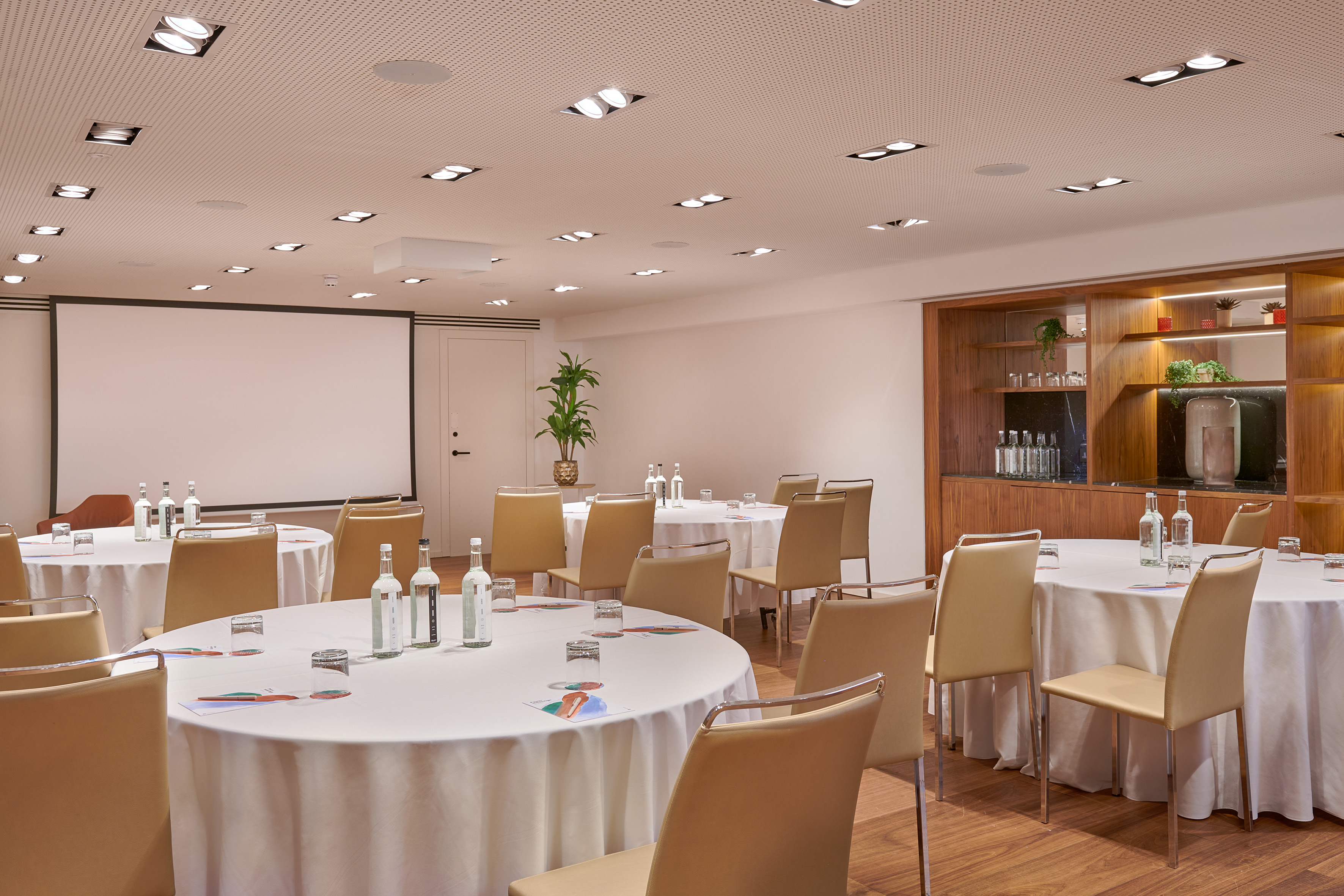 Modern conference room with round tables, projection screen, and beverage bar.