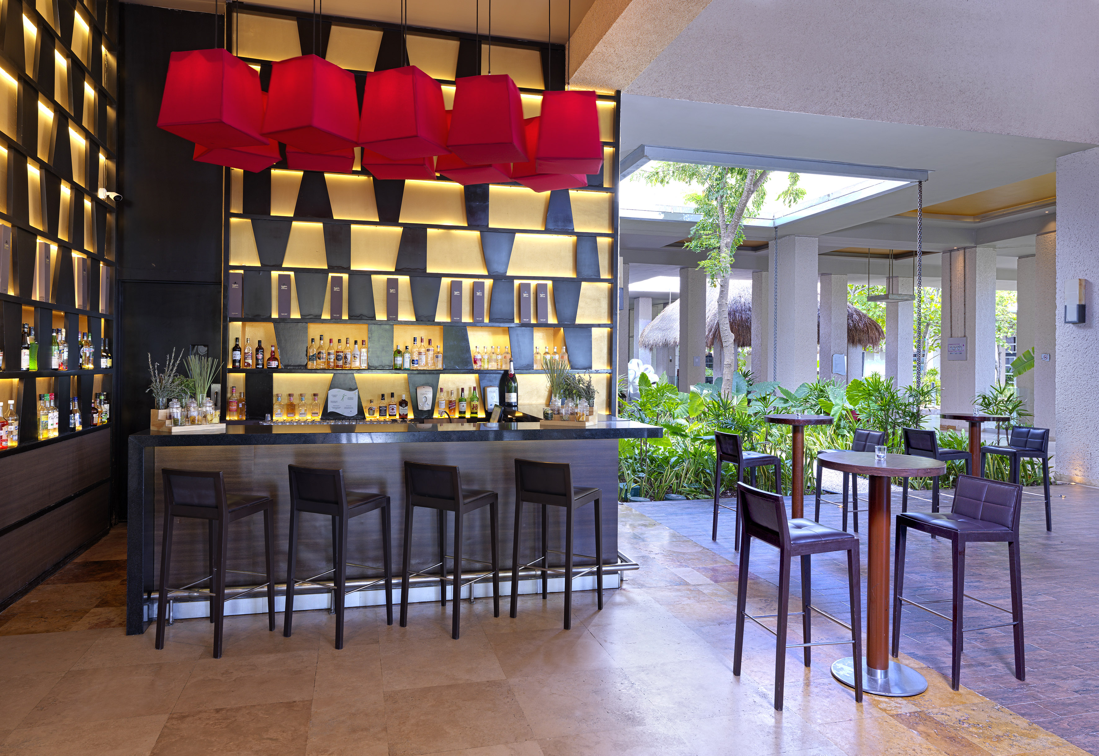 Modern bar with red pendant lights, backlit liquor shelves, and outdoor patio.