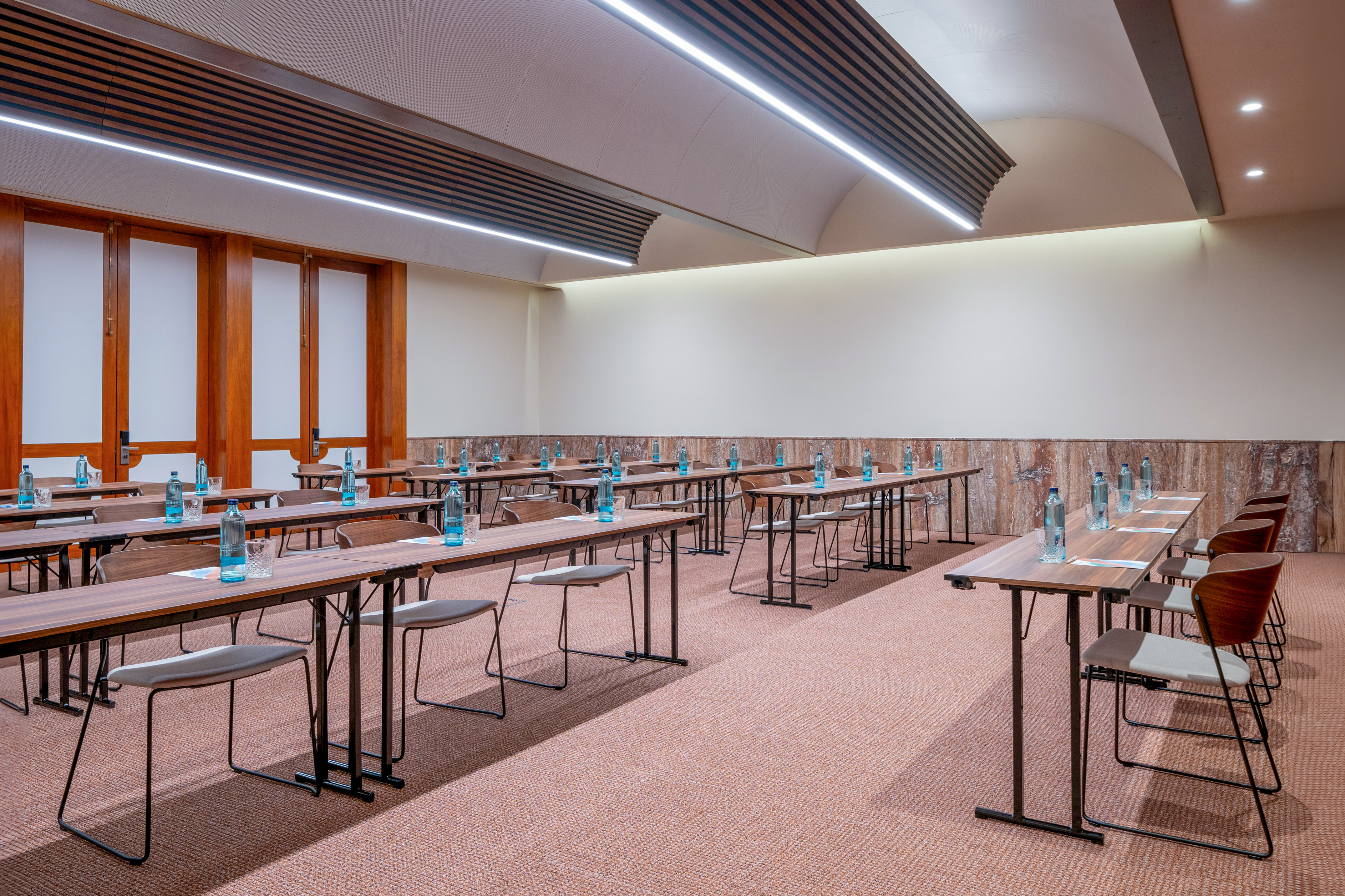 Modern conference room setup with tables, chairs, water, and linear lighting.