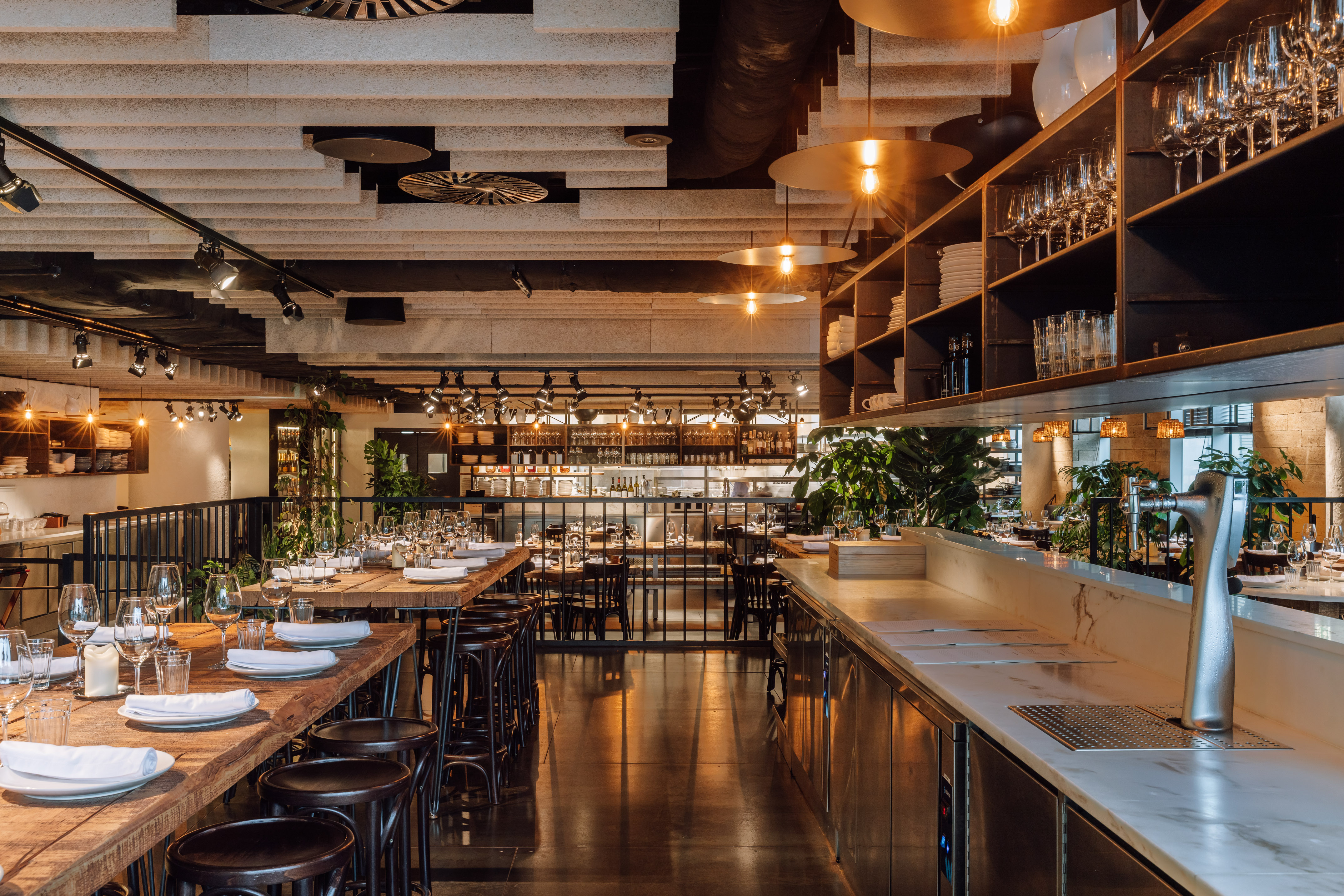 Modern restaurant design with long wooden tables, bar, and industrial lighting.